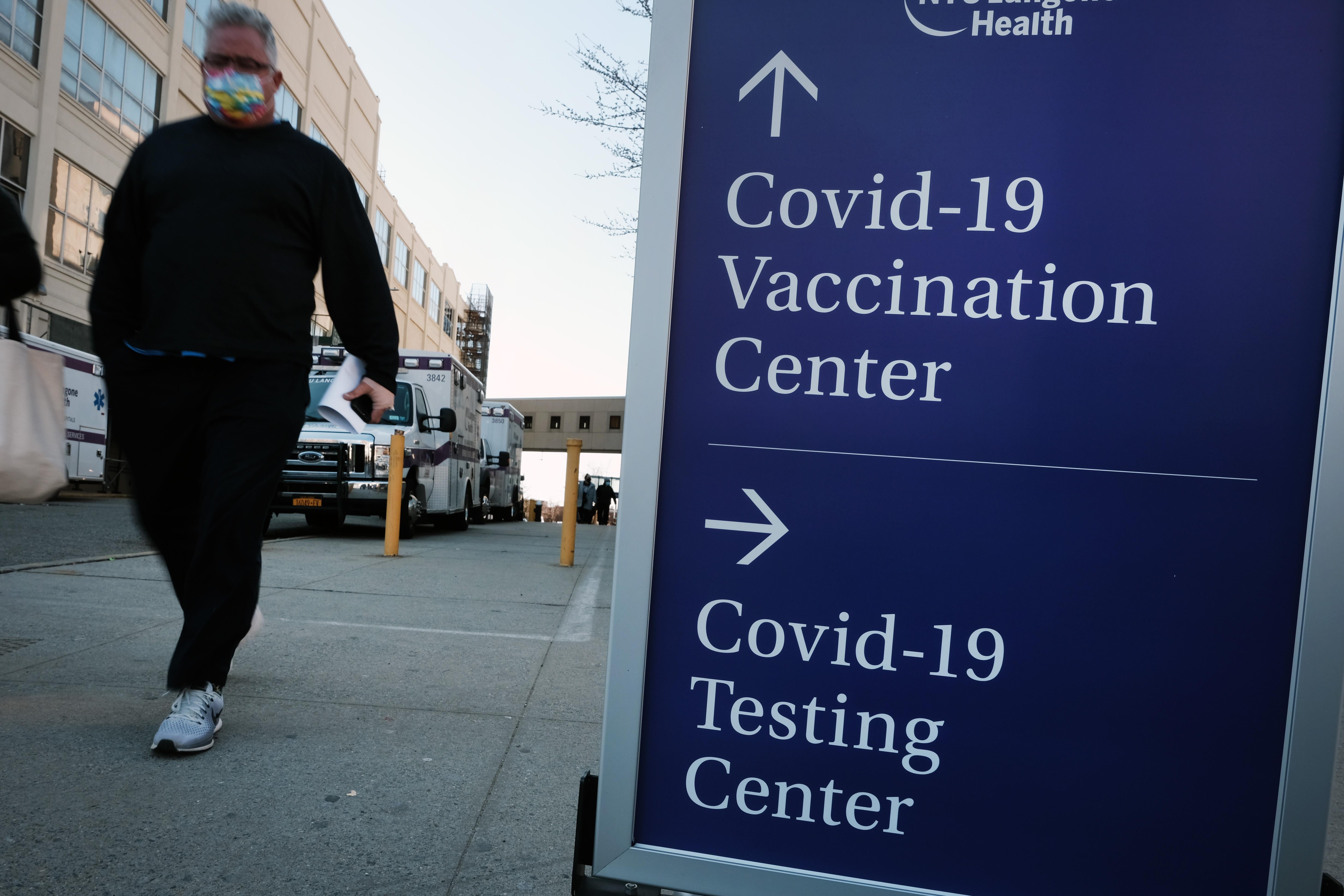 People walk by a sign pointing toward a COVID-19 testing center and a COVID-19 vaccination center at a Brooklyn hospital.