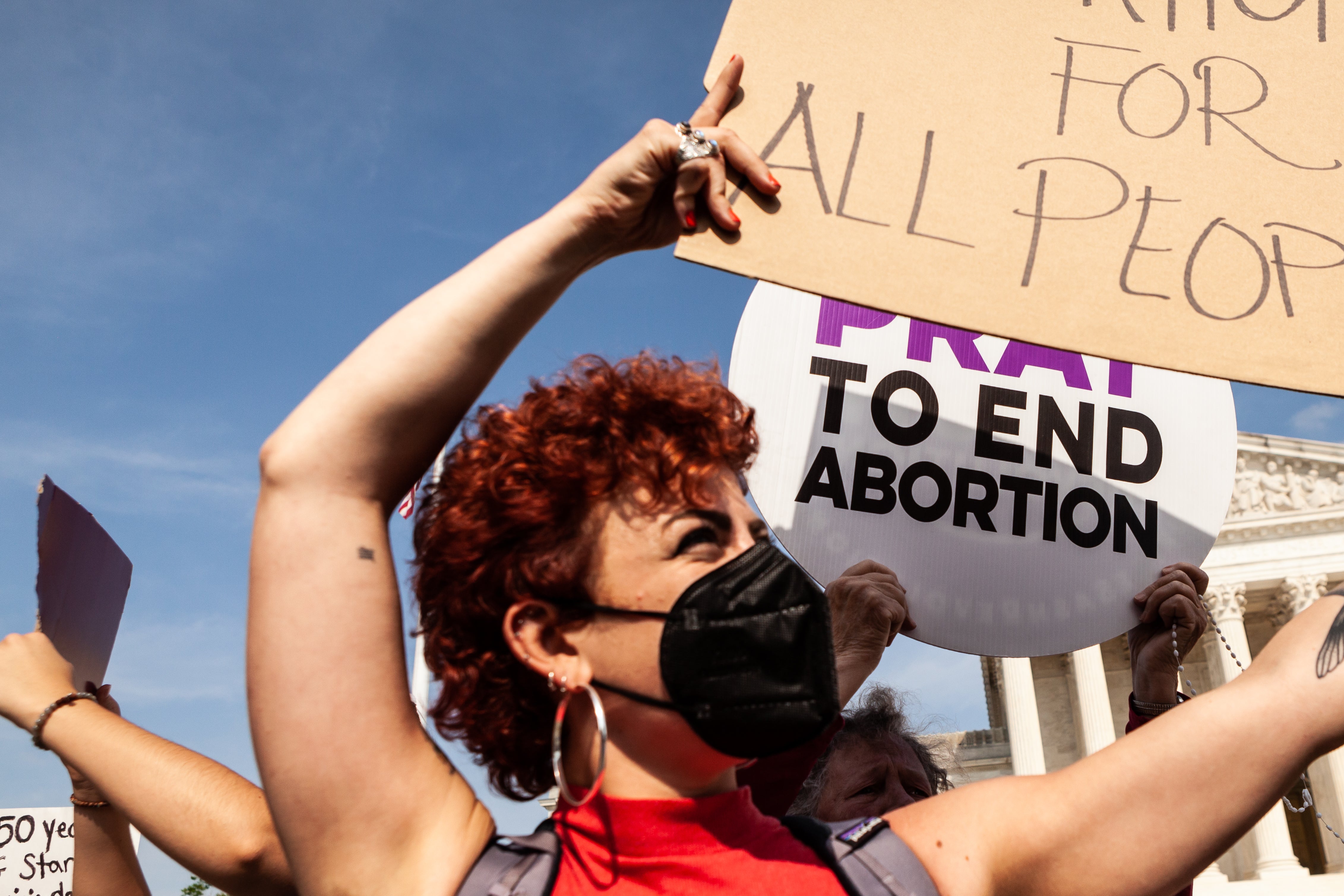 A pro-choice protester holds a sign in front of an anti-abortion protester holding a sign that says "Pray to End Abortion" outside the Supreme Court.