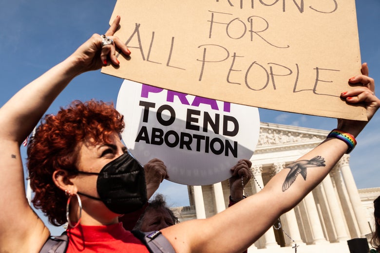 A pro-choice protester holds a sign in front of an anti-abortion protester holding a sign that says "Pray to End Abortion" outside the Supreme Court.