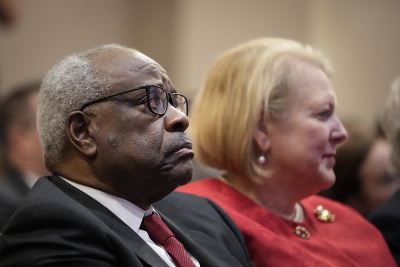 Clarence Thomas in a suit and Ginni Thomas in a red dress sitting next to each other in the audience