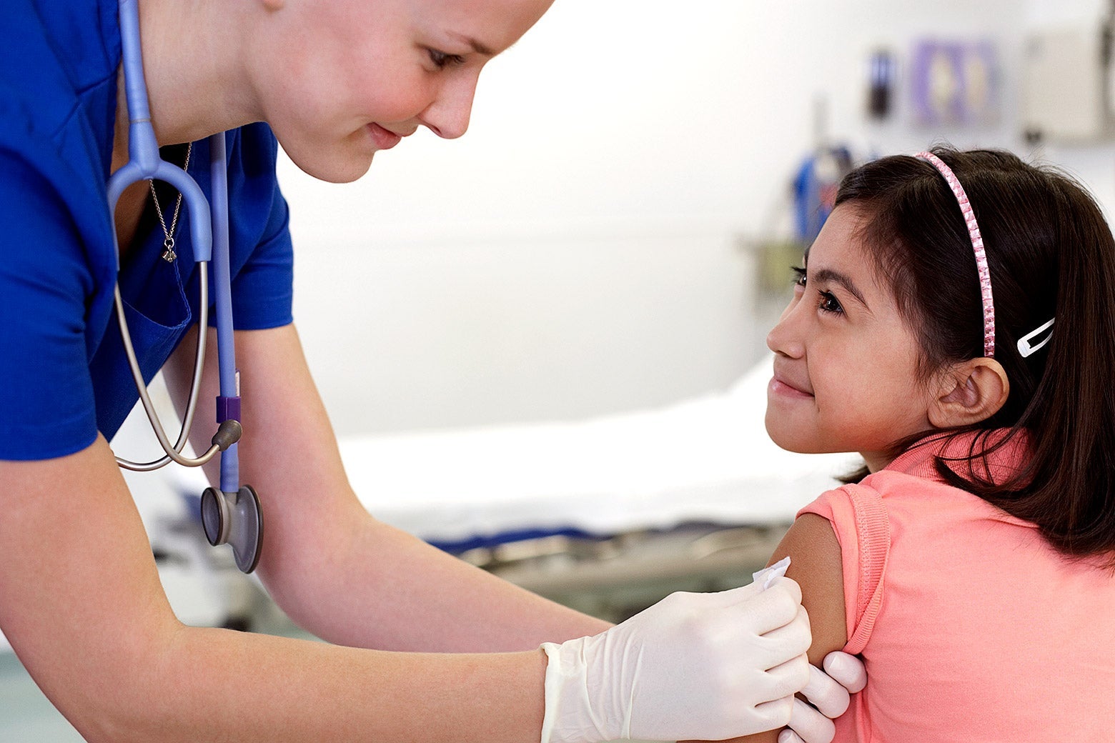 A health care provider puts a bandage on a child’s arm where she might have just gotten a shot.