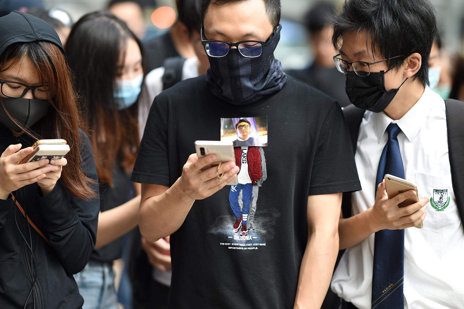 Protesters, wearing masks to cover their faces, look at their smartphones.