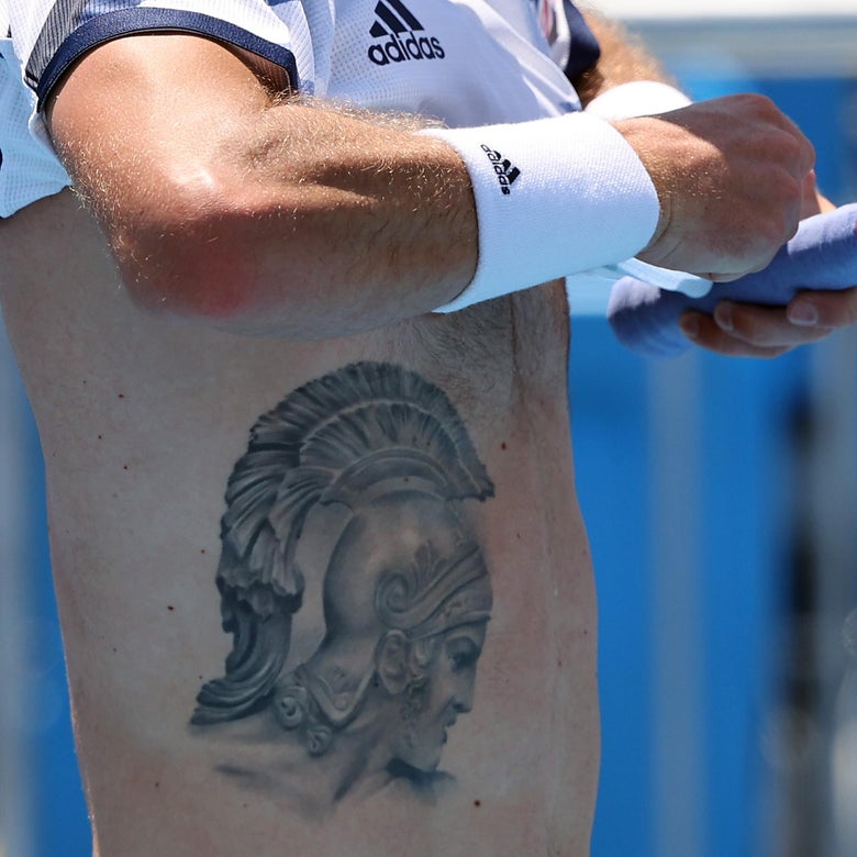 A man in Adidas wristband and holding a purple tennis-racket handle in his left hand lifts up his Adidas shirt, revealing the Achilles-in-helmet tattoo