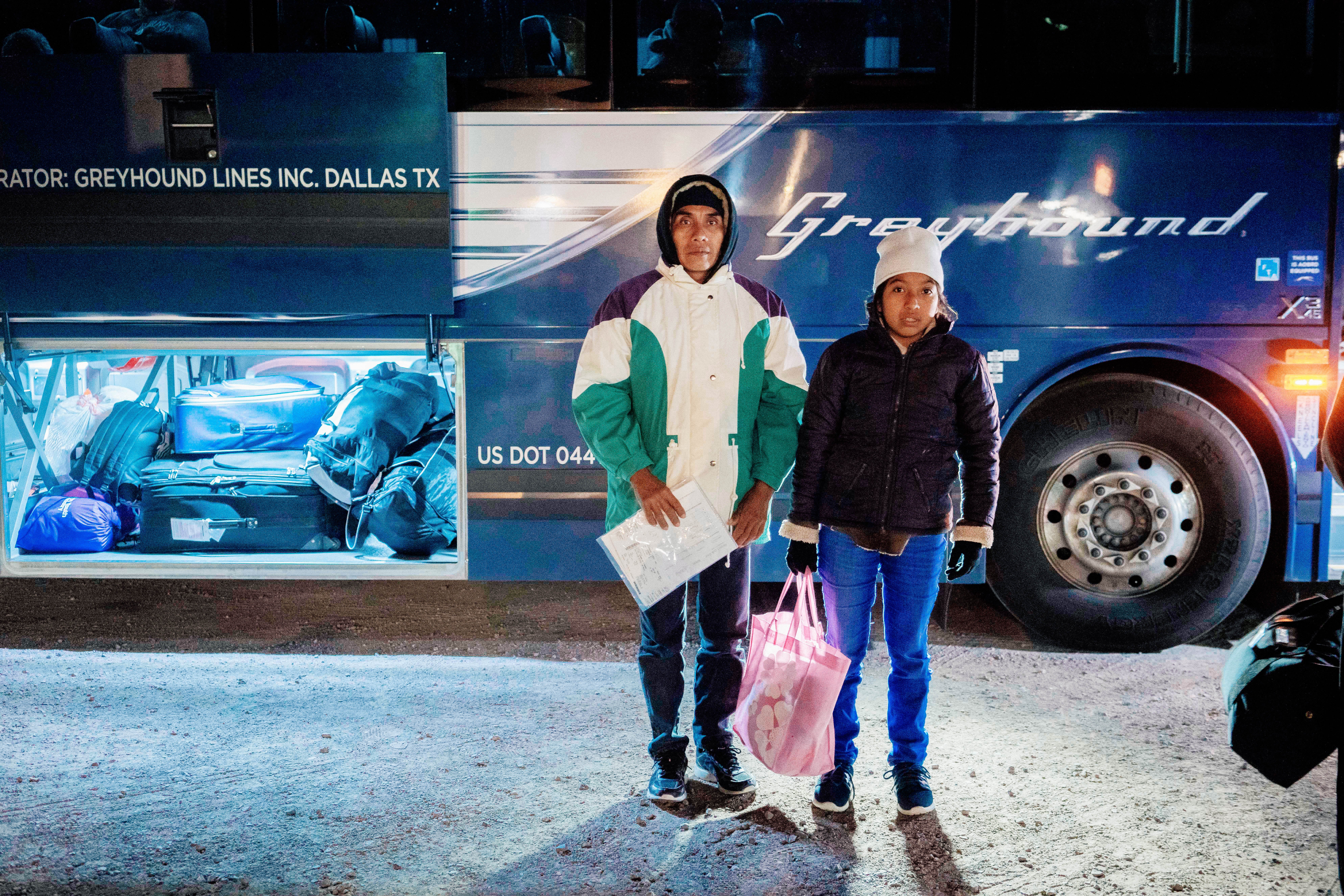 A man and his daughter stand in front of a Greyhound bus.