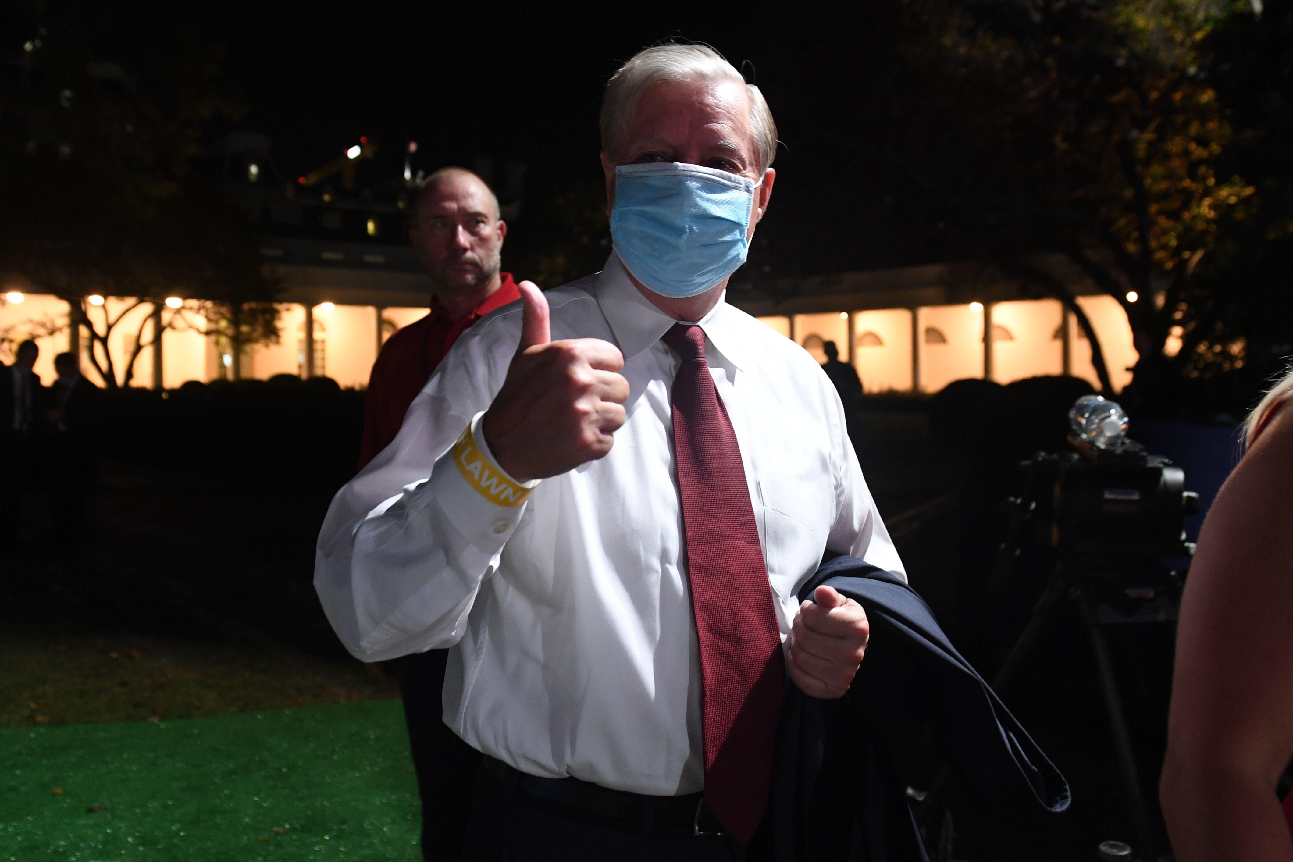 Graham, wearing a mask, gives a thumbs-up outside the White House at night