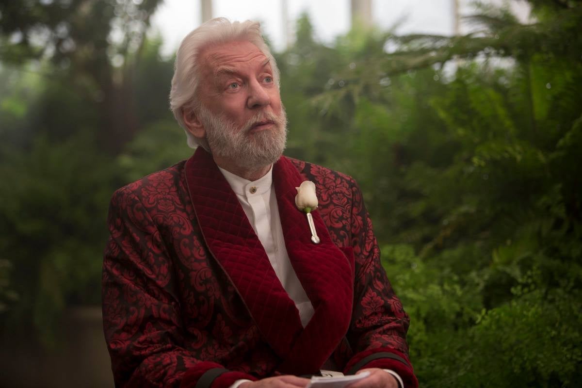 Snow has white hair, a white beard, and a white rose tucked into his lapel.