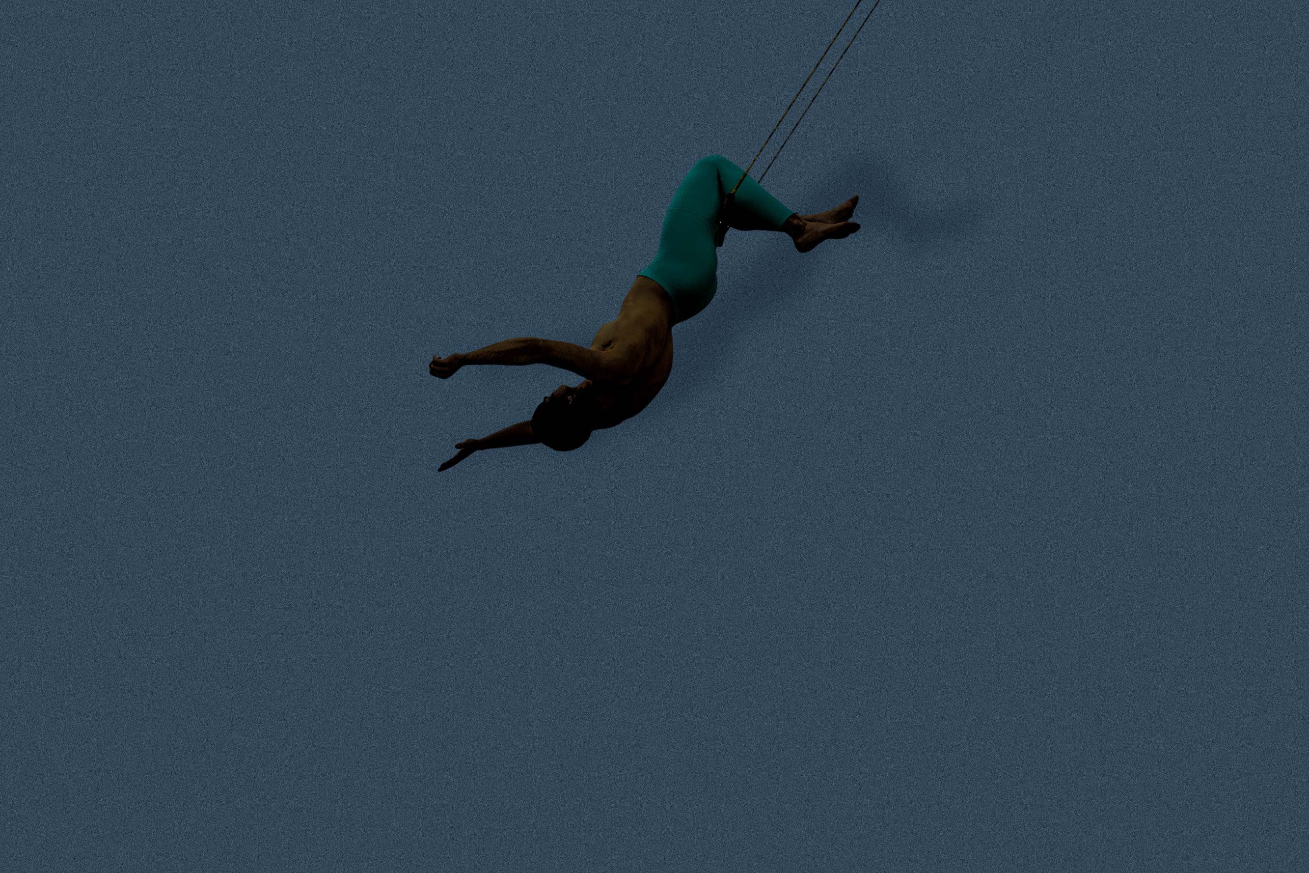 A man hangs by his knees from the flying trapeze.