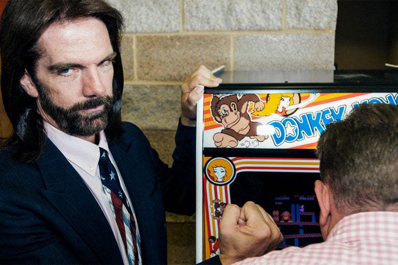 Billy Mitchell poses next to a Donkey Kong game console, 2009.