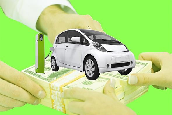 A car at a charging station is seen on bundles of $100 bills being held by two pairs of hands.