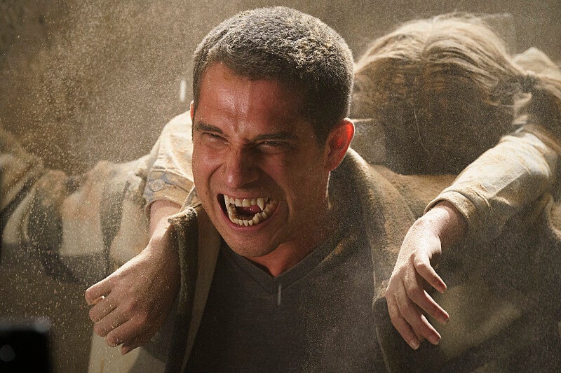 A man carries a girl, covered in dust, with fangs showing. 