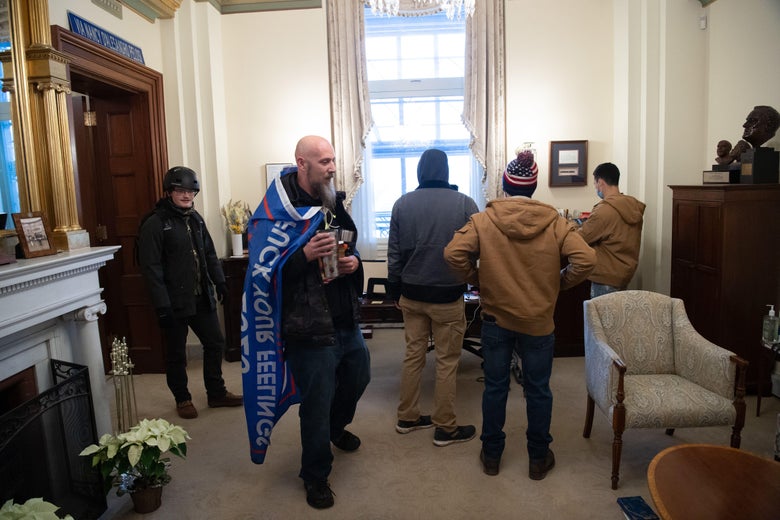 A man draped in a flag that says "Fuck Your Feelings" stands in an office with four other men