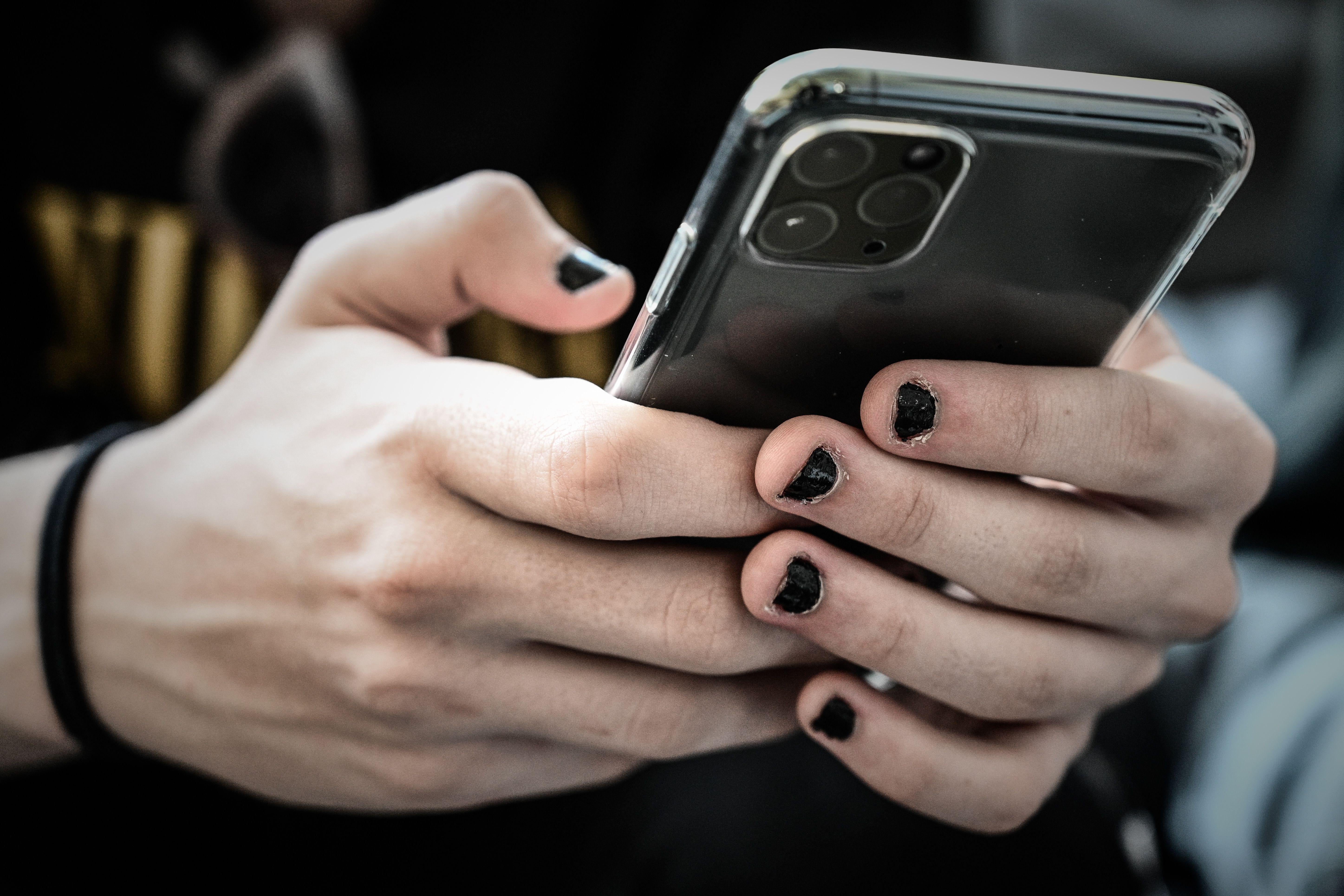 Two hands with black nail polish use an iPhone