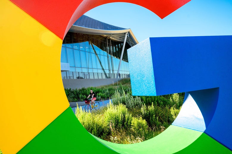 A bicyclist rides by a glass-and-metal building; it's viewed through Google's red, yellow, green, and blue G.