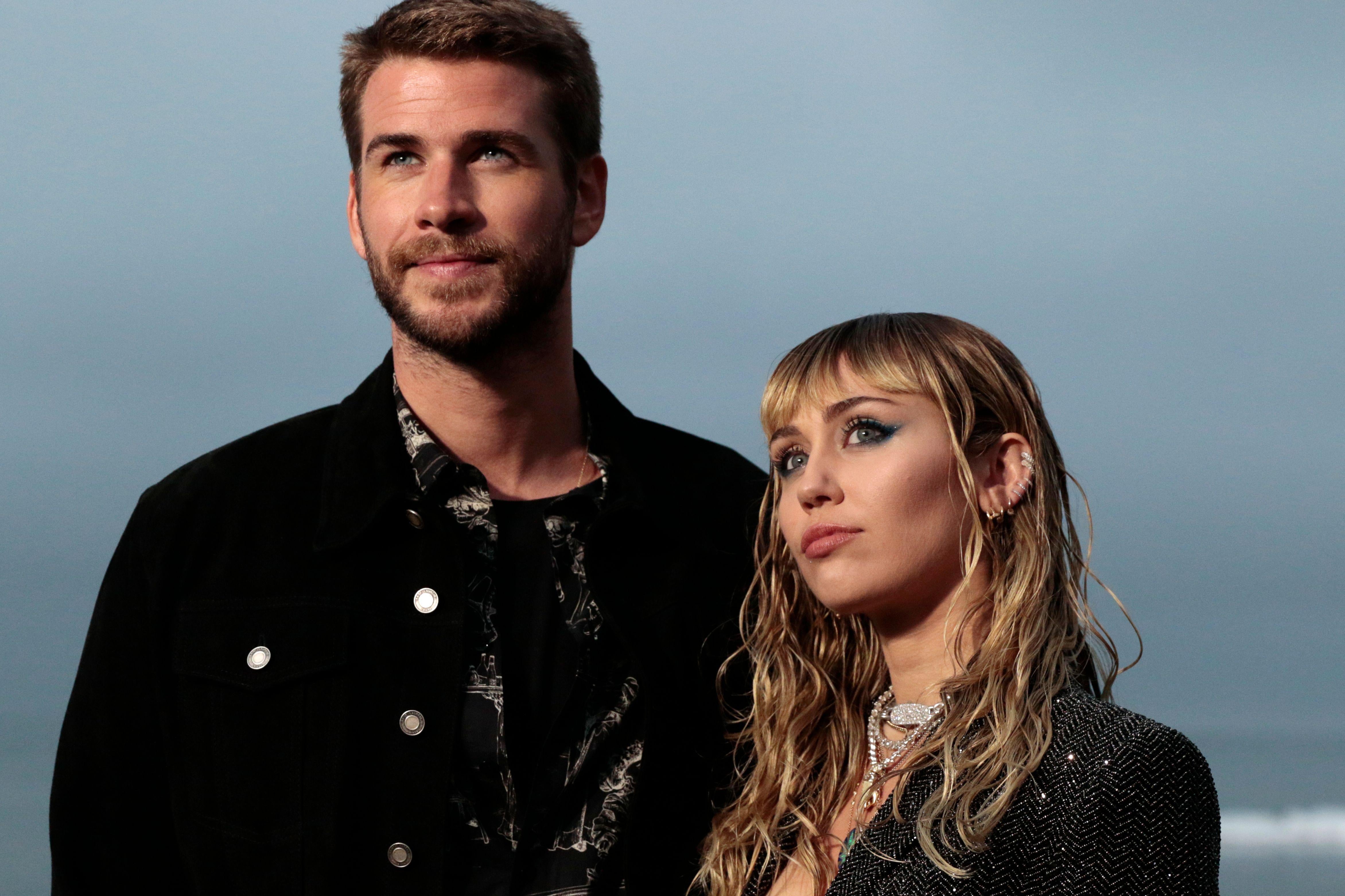 Liam Hemsworth and Miley Cyrus looking thoughtful, with an ocean in the background.