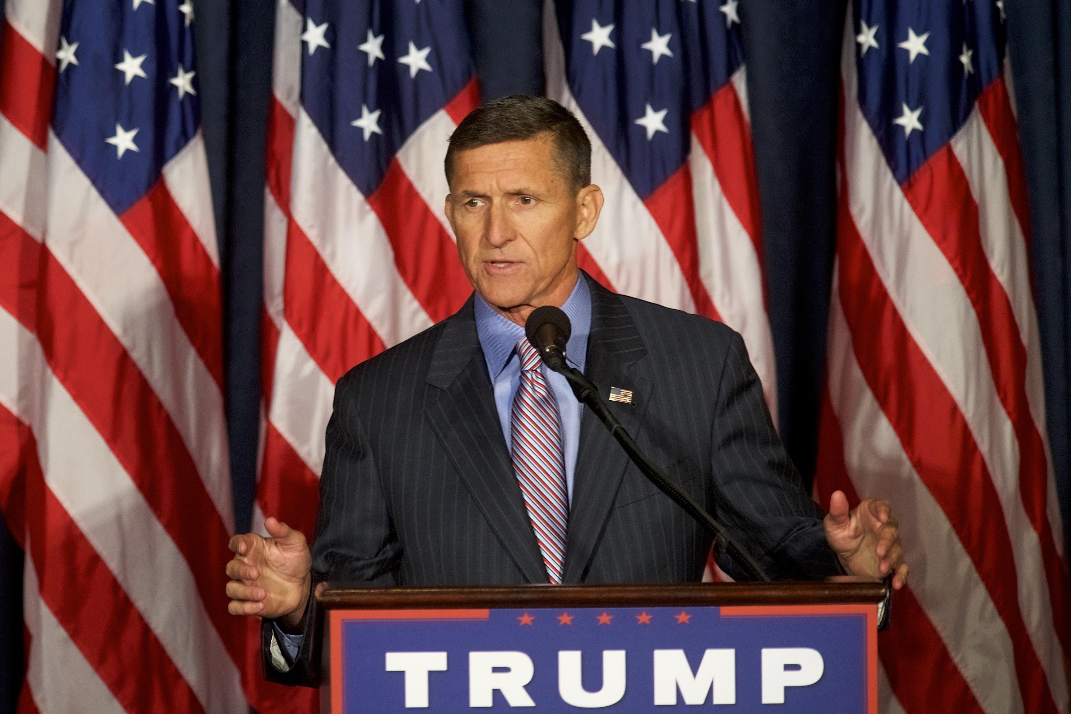 Michael Flynn speaks at a podium with a Trump campaign sign on the front. 
