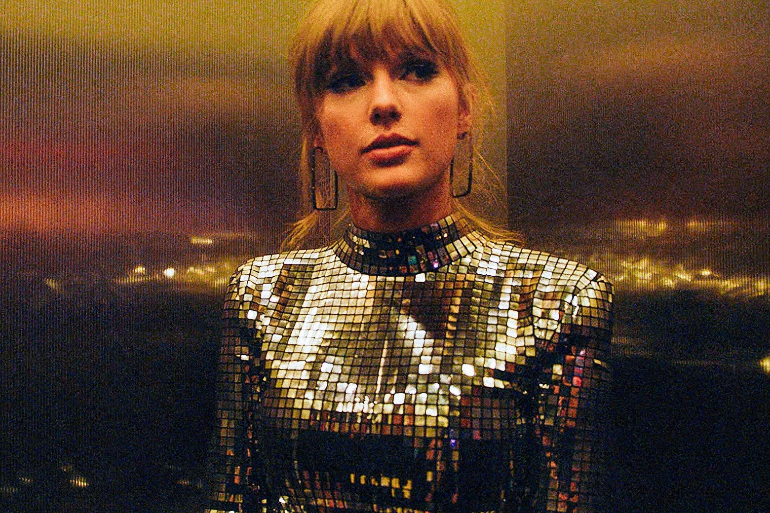 Taylor Swift in an elevator, looking like she's wearing a mirrorball for a shirt