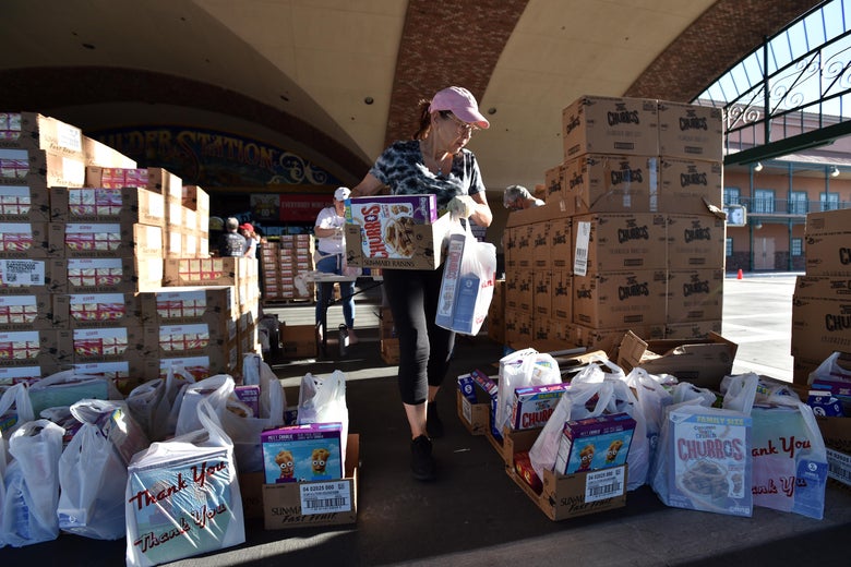 Volunteers prepare bags of groceries for distribution, walking among stacks and stacks of food boxes