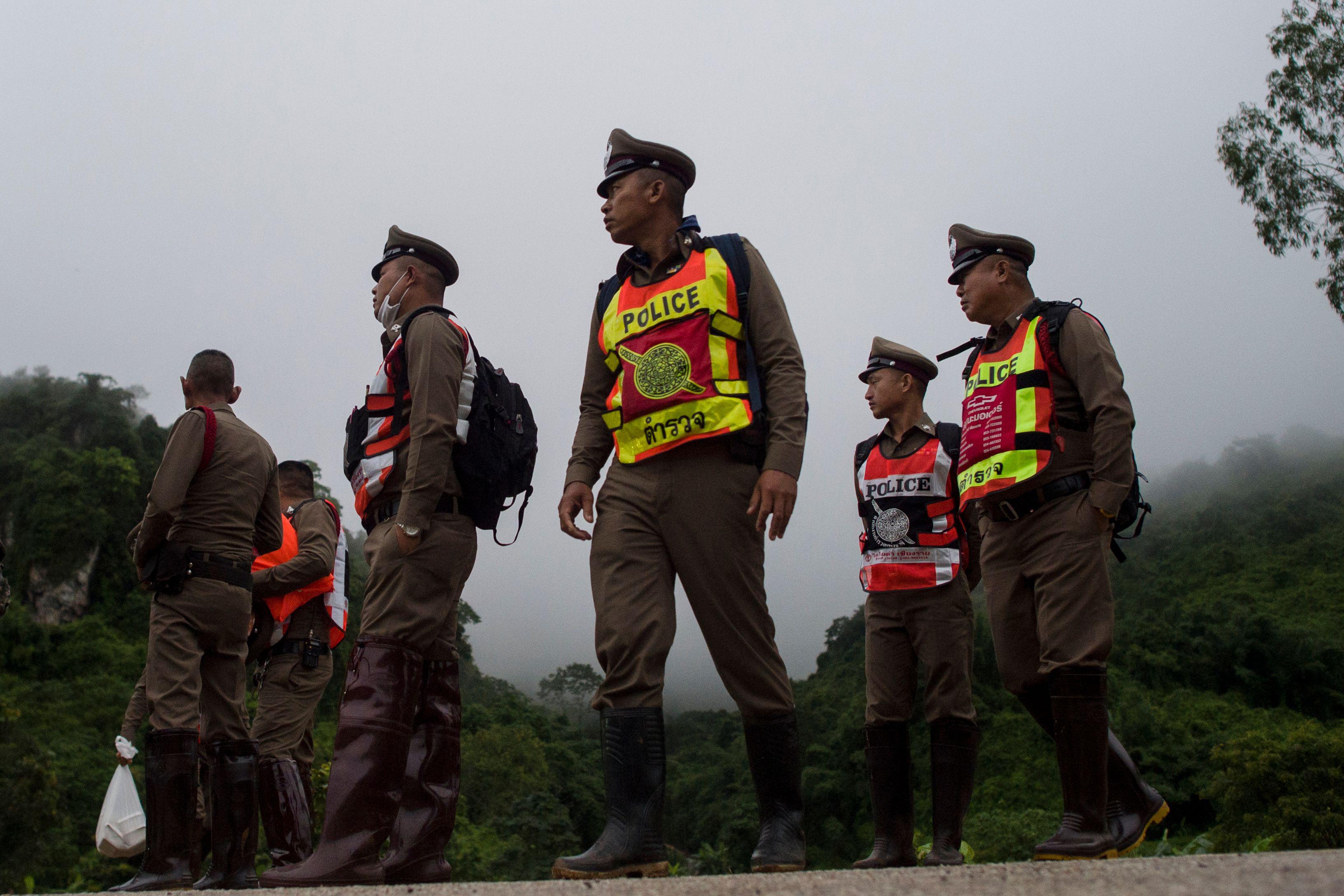 Thai police, wearing bright yellow and orange vests over their brown hats and uniforms