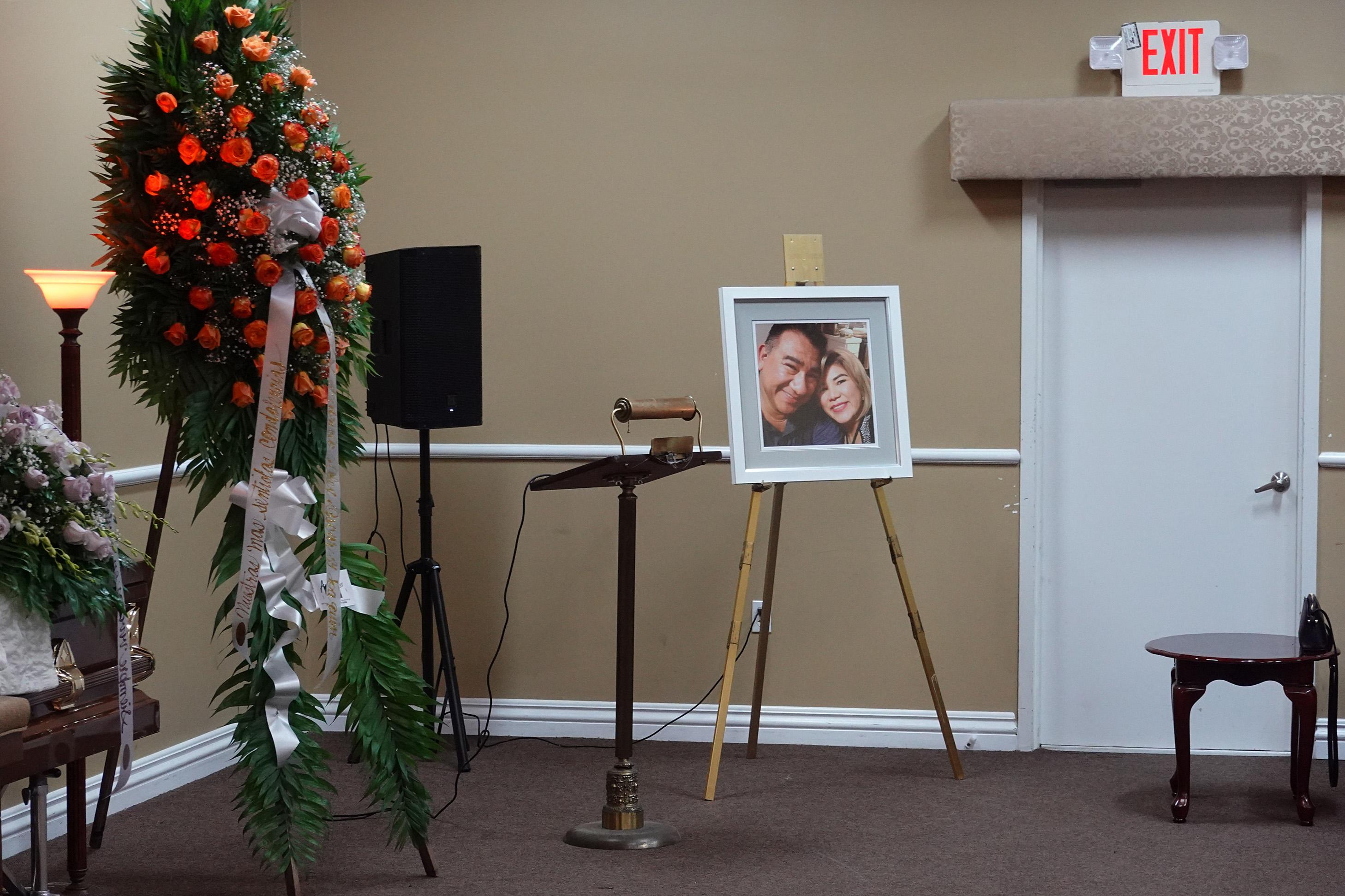 A picture of a couple beside a lectern and flowers in a room empty of people.