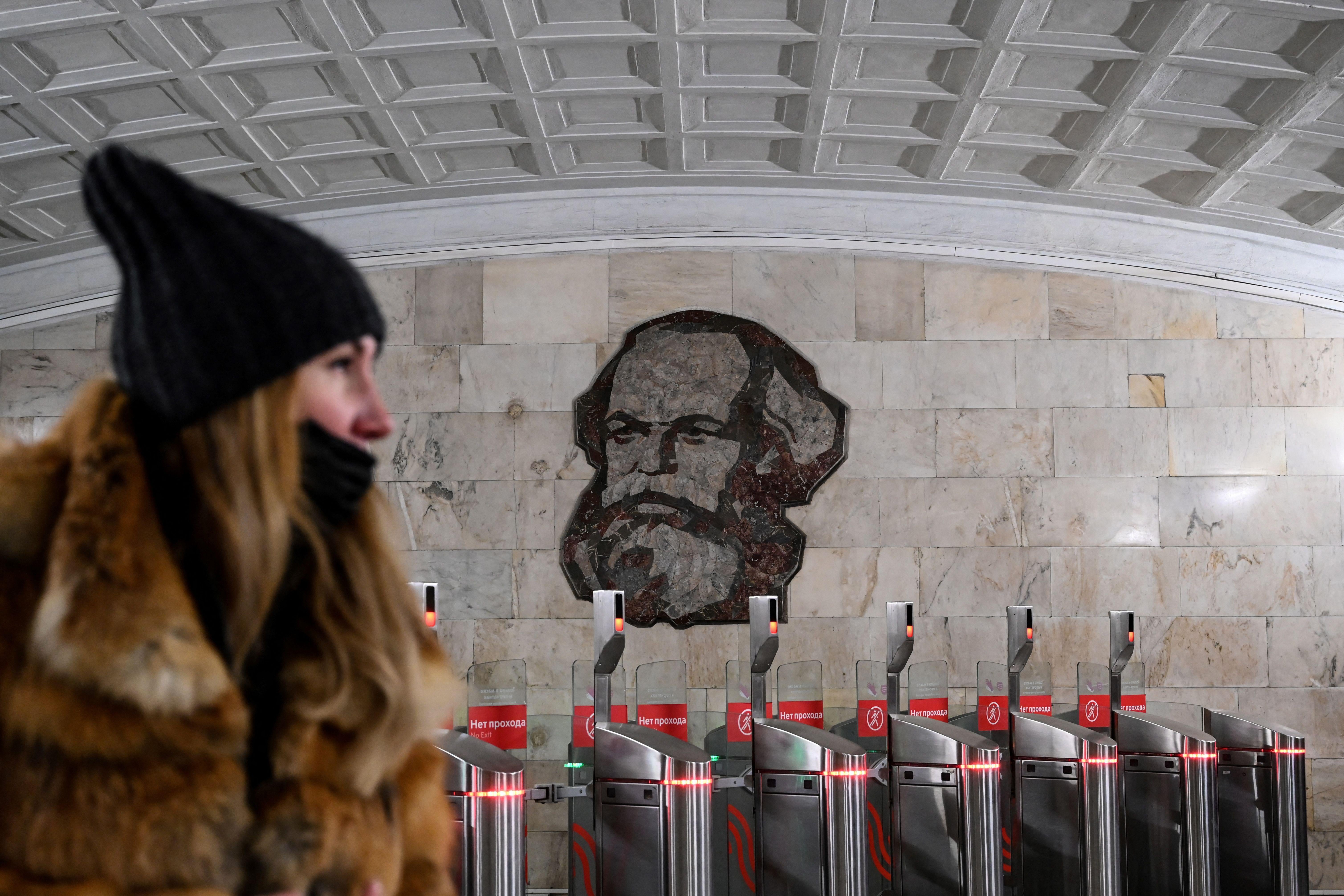 A woman wearing a face mask walks in front of an image of German philosopher and economist Karl Marx in subway in Moscow on March 12, 2021.