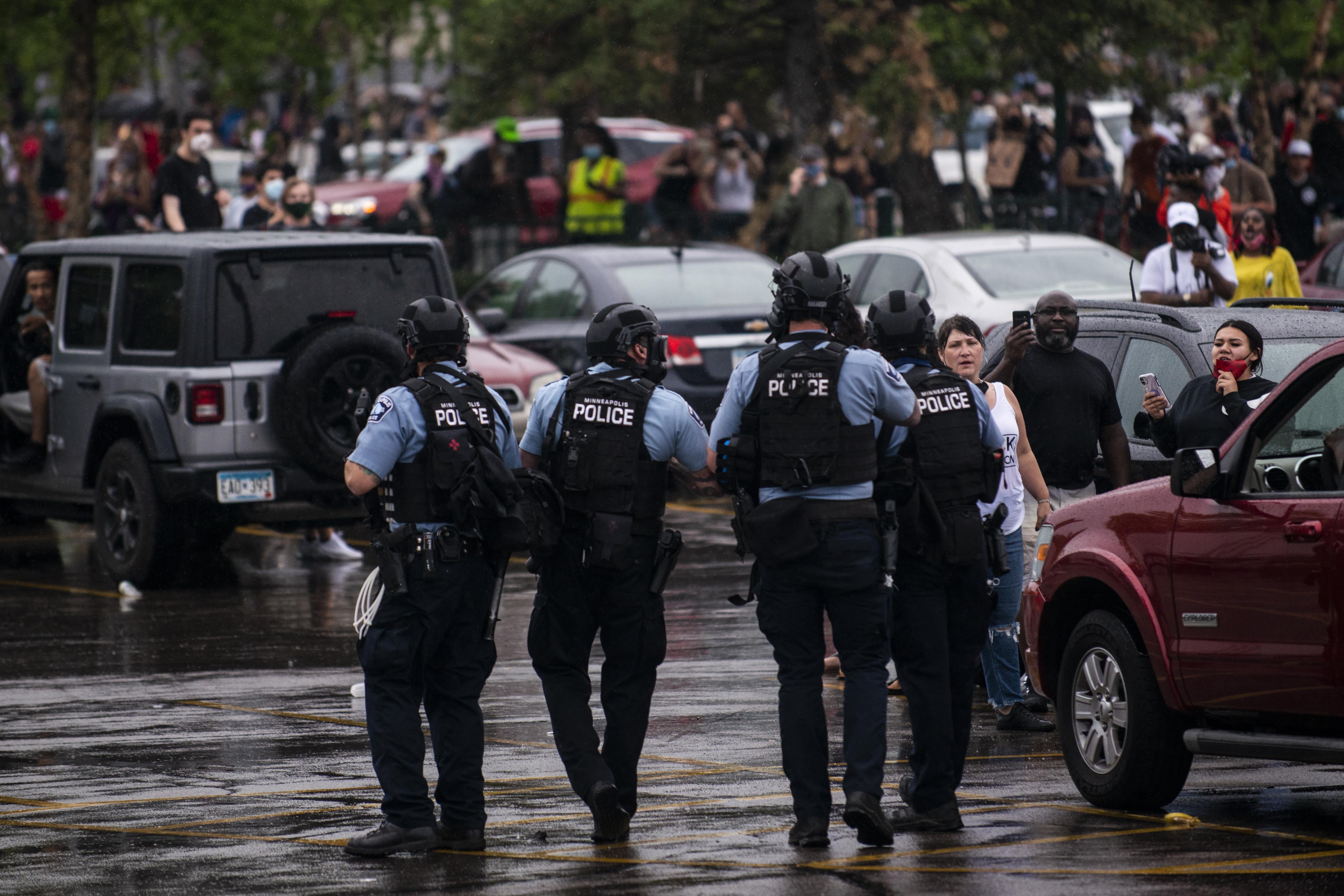 Police wearing tactical gear walk through a parking lot toward a crowd of protesters