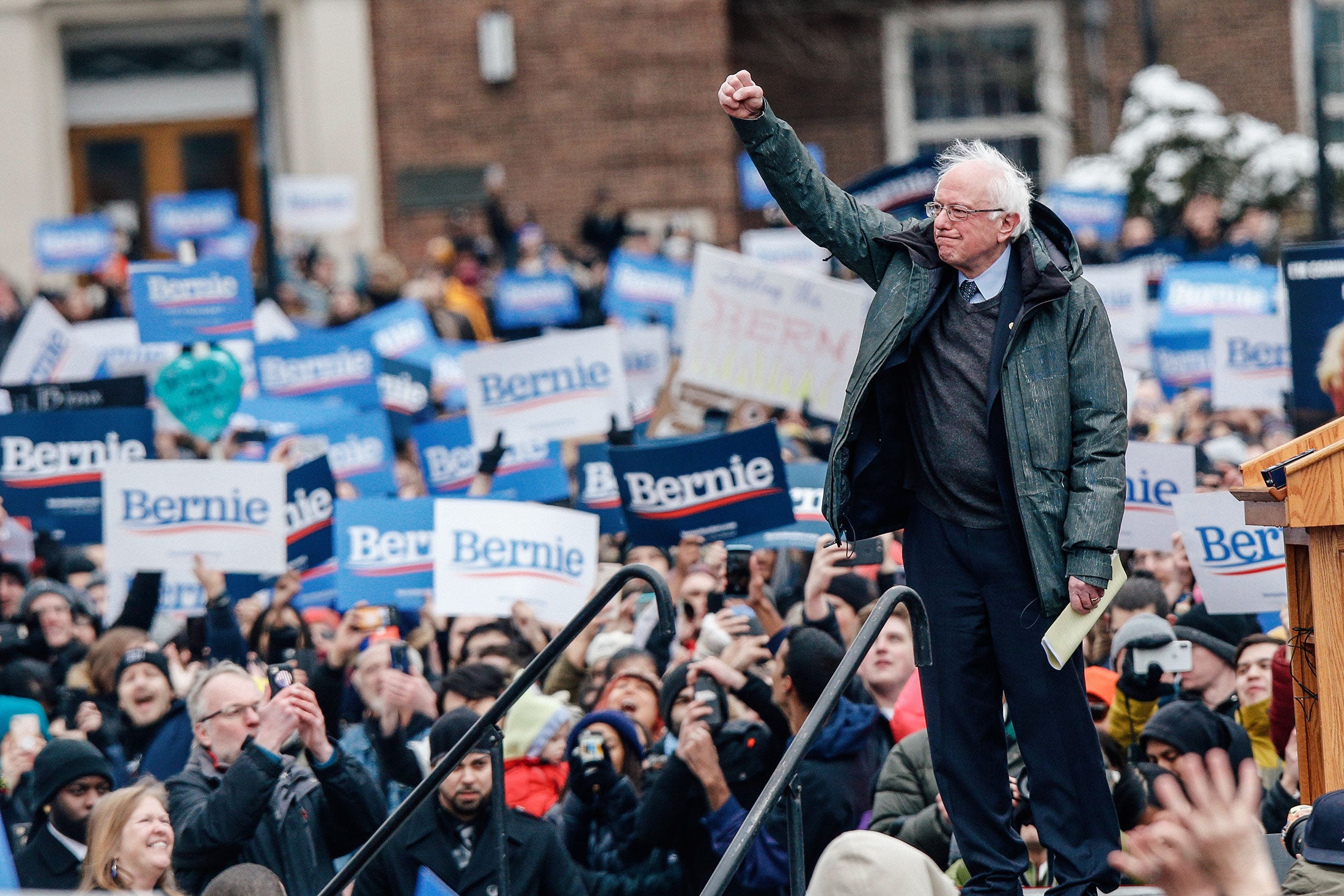 Bernie Sanders raising a fist of solidarity surrounded by campaign supporters.