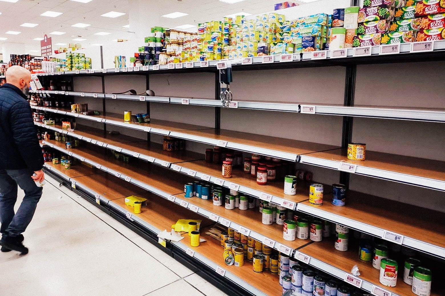 A man stares at an empty canned goods aisle in the grocery store, with just a few choices left.