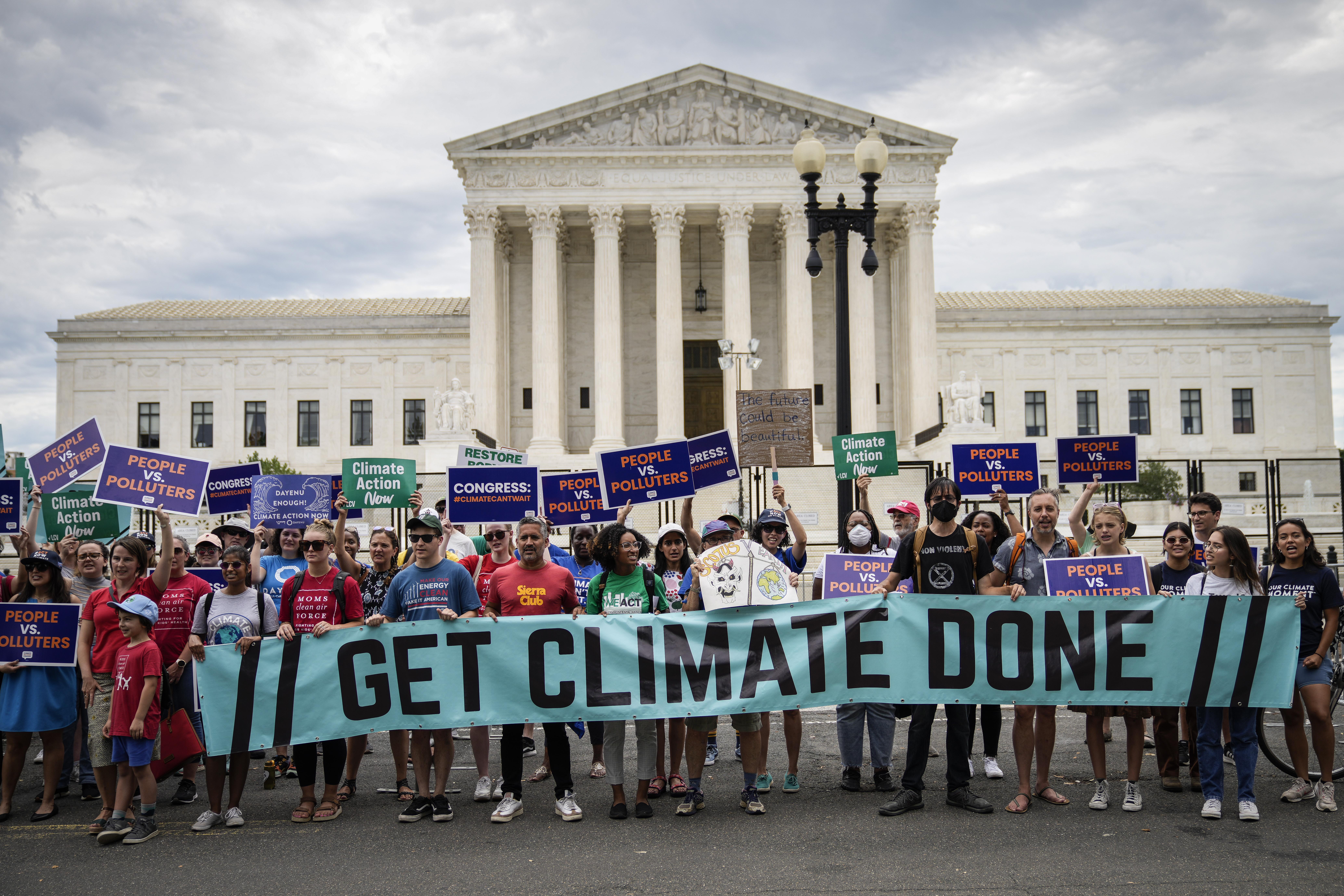 A line of about 20 environmental activists stand in front of the U.S. Supreme Court holding a light blue banner that says "Get Climate Done." They are also holding other climate-related signs. 