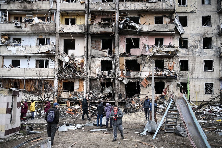 A bombed-out apartment building with people standing out front.