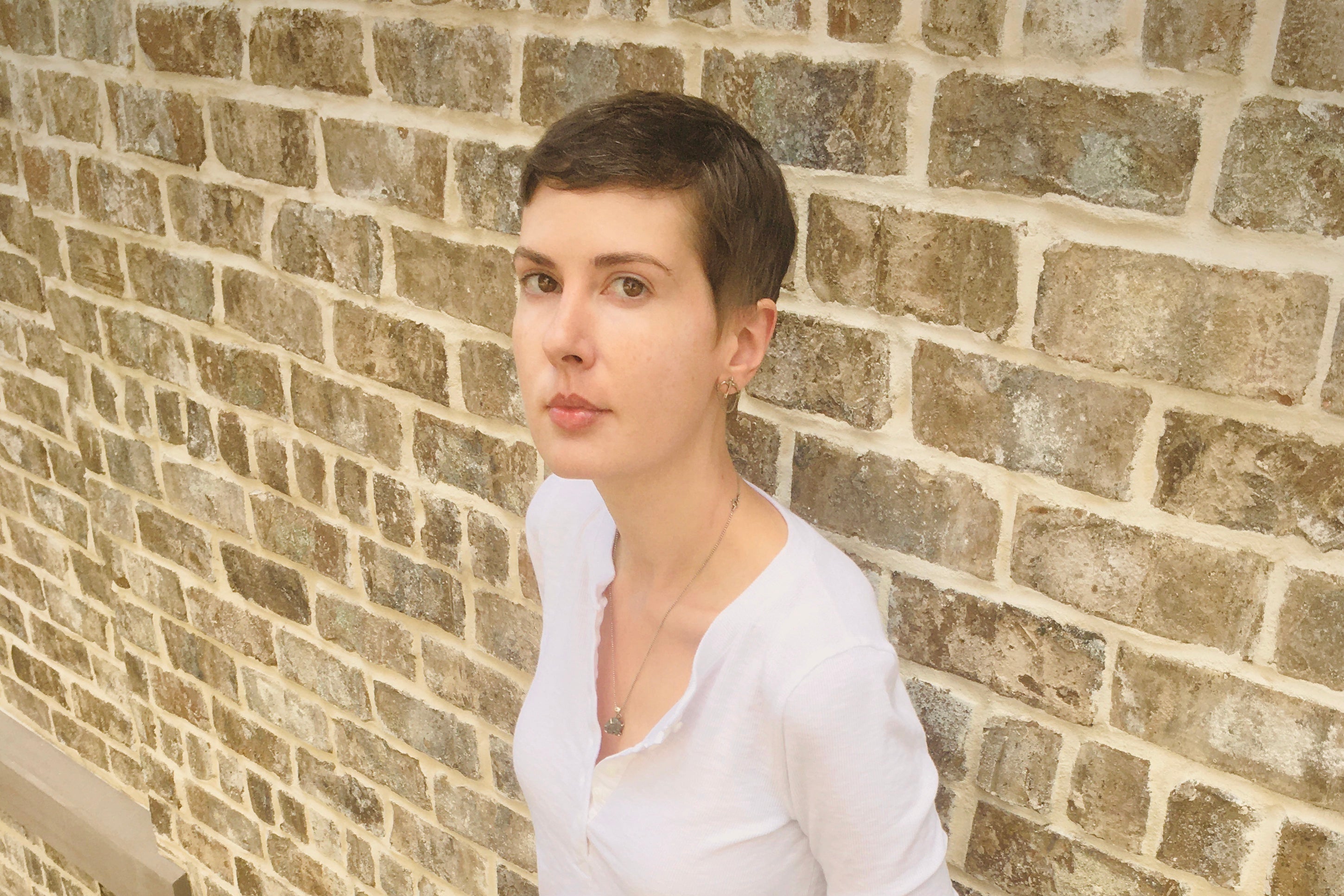 A woman in a white shirt leans against a brick wall.