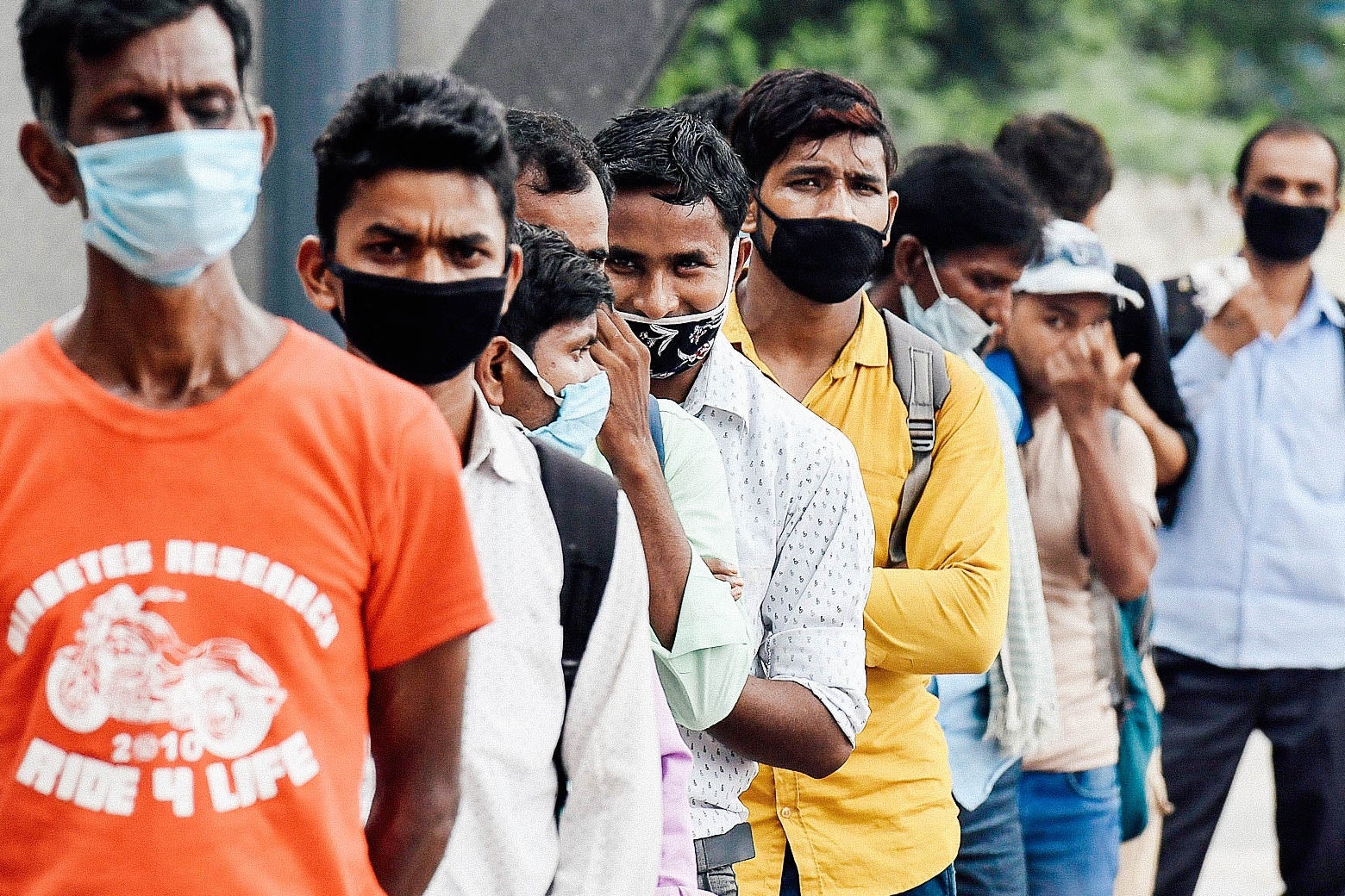 Men wearing masks stand in a queue.