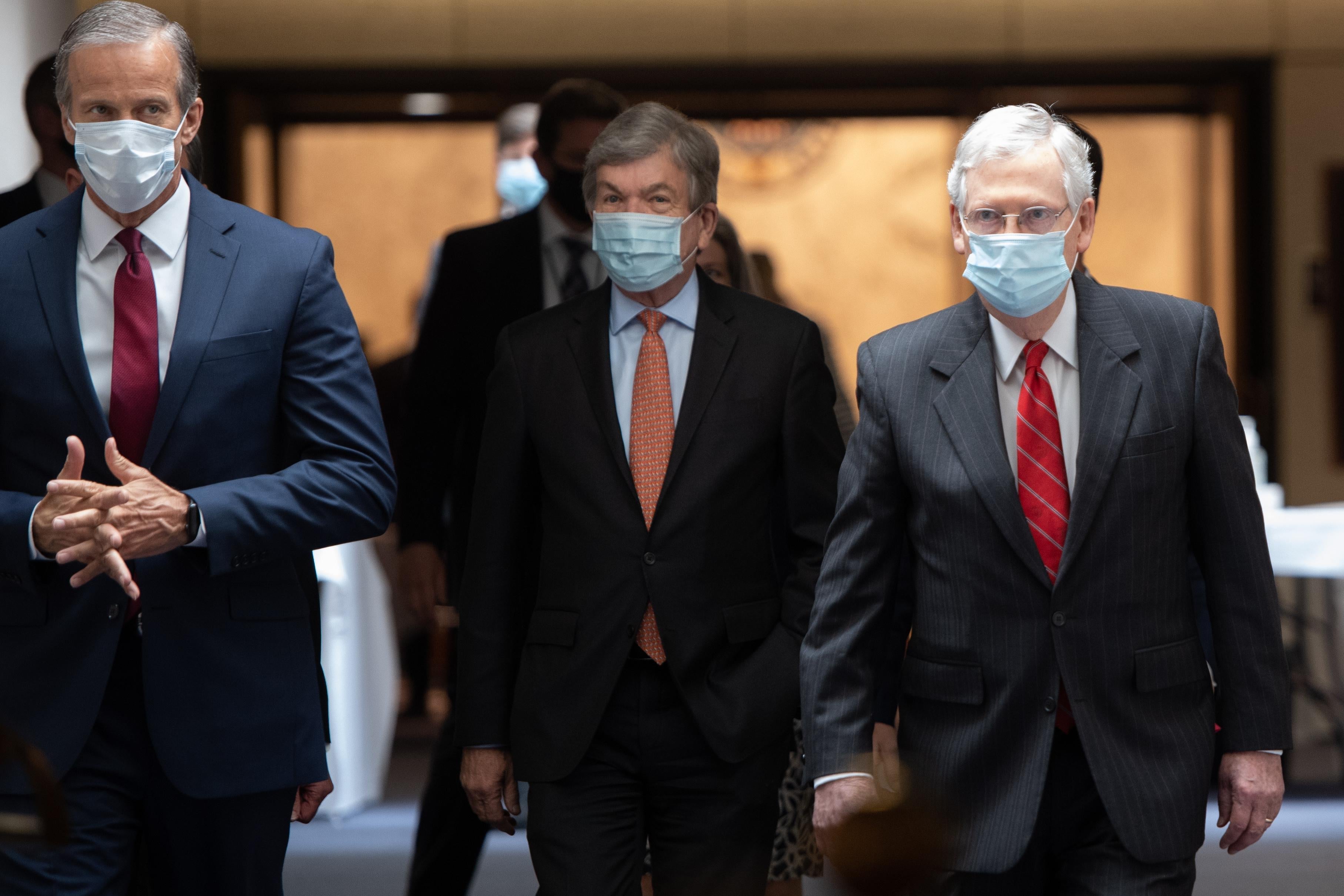 Three men in suits and face masks are walking