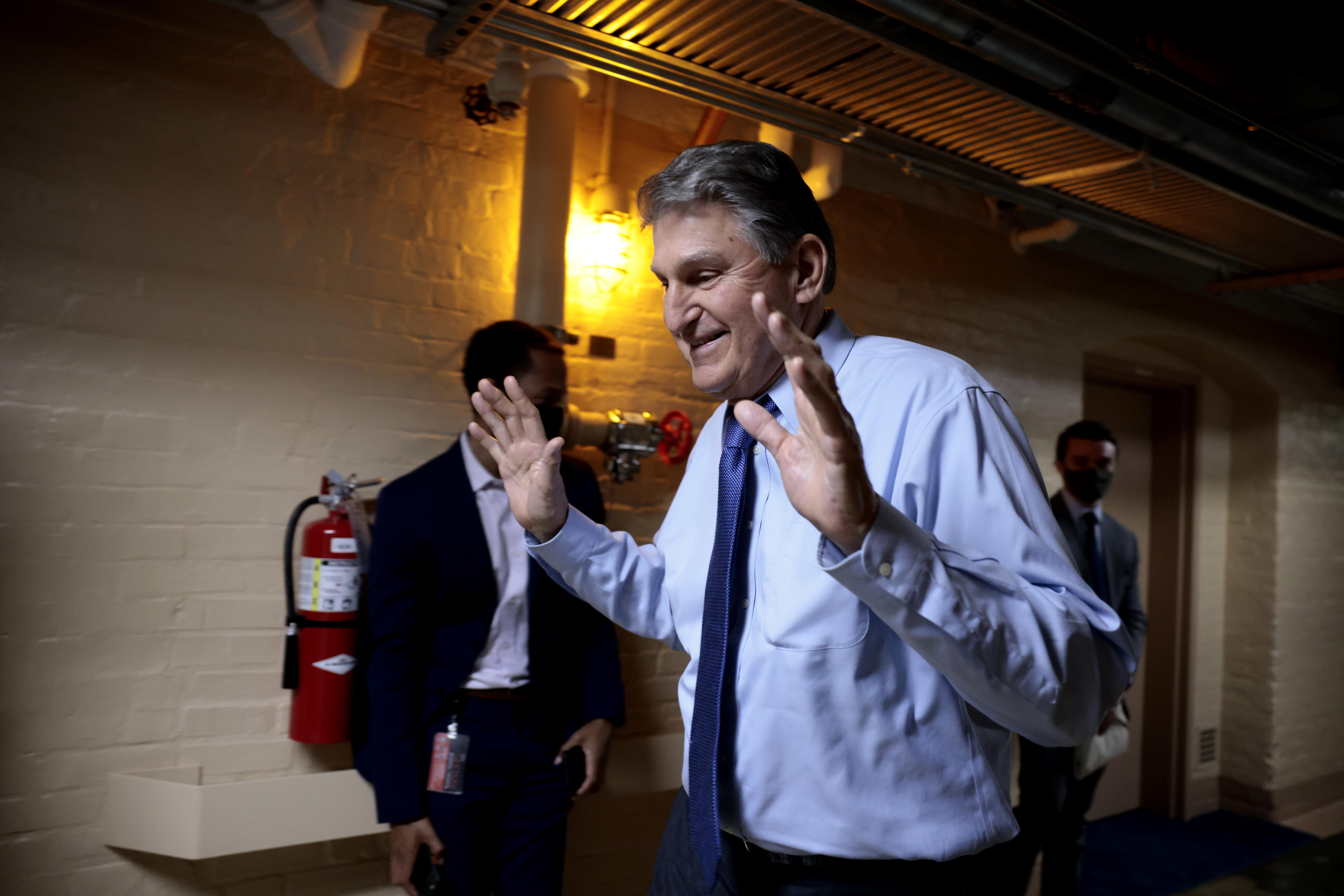 Sen. Joe Manchin walking down a hallway in the basement of the U.S. Capitol Building, with a smile on his face and his hands thrown up in the air. 