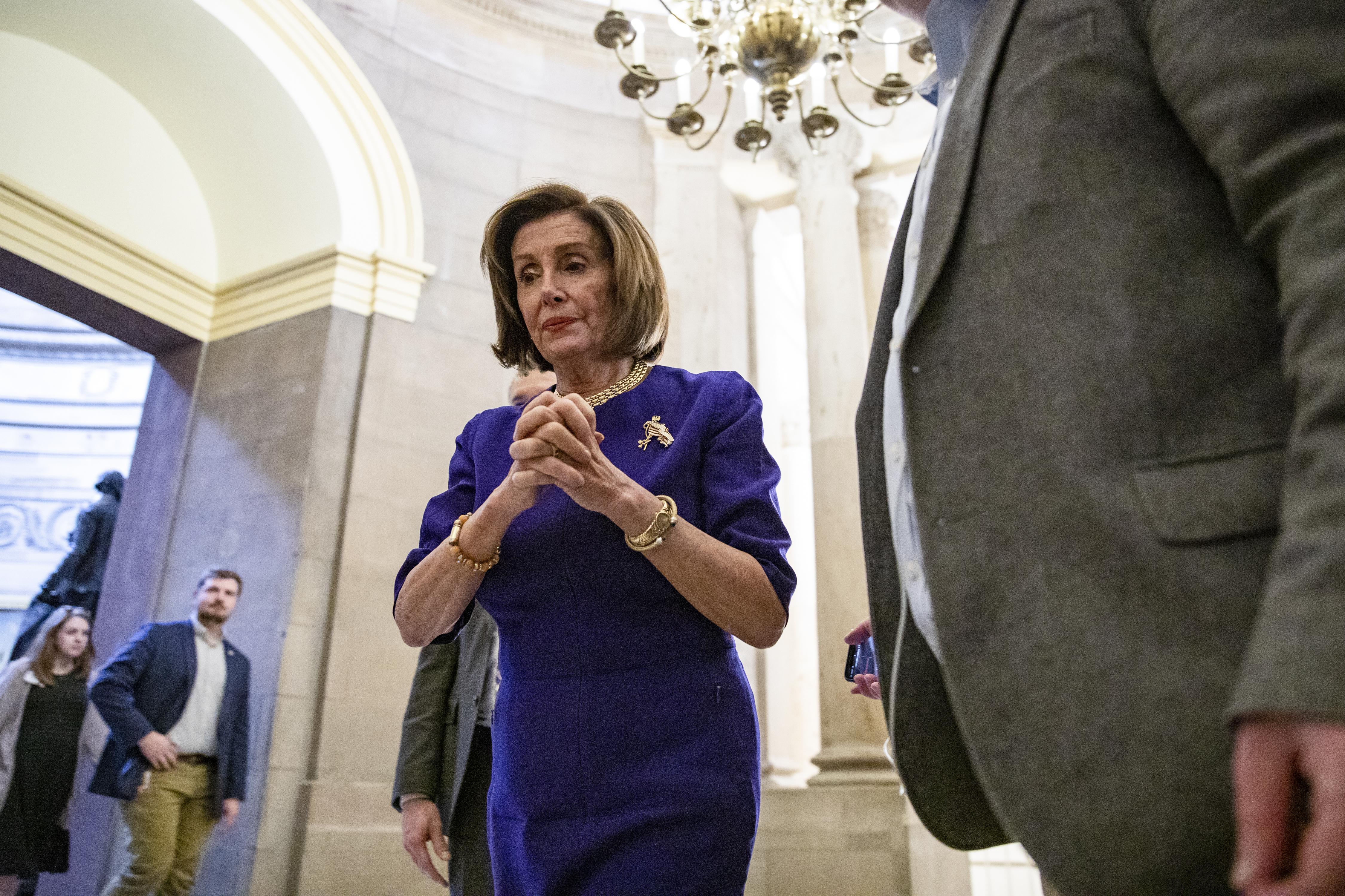 Nancy Pelosi walks with her hands clasped.