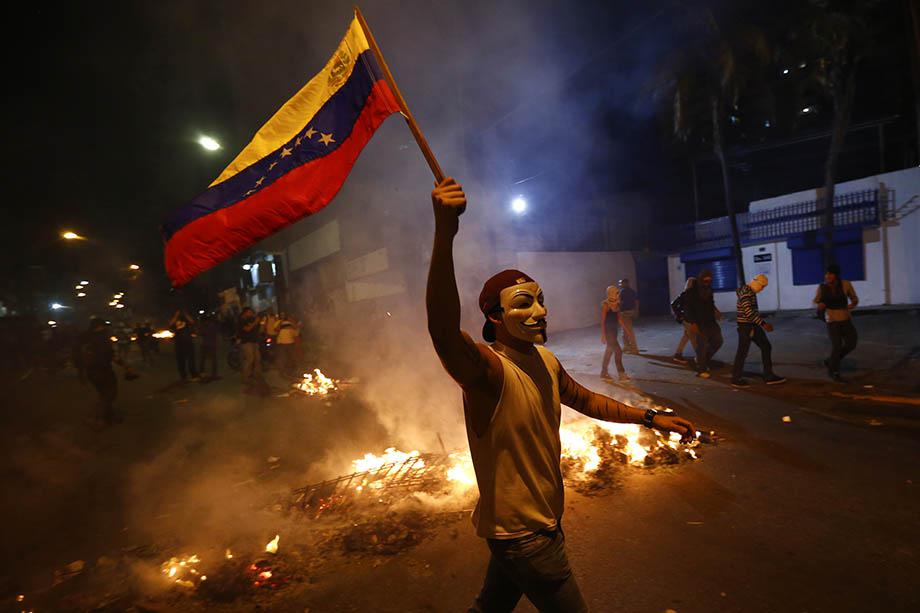 An opposition demonstrators holds a Venezuelan flag in front of a burning barricade during a protest against President Nicolas Maduro's government in Caracas.