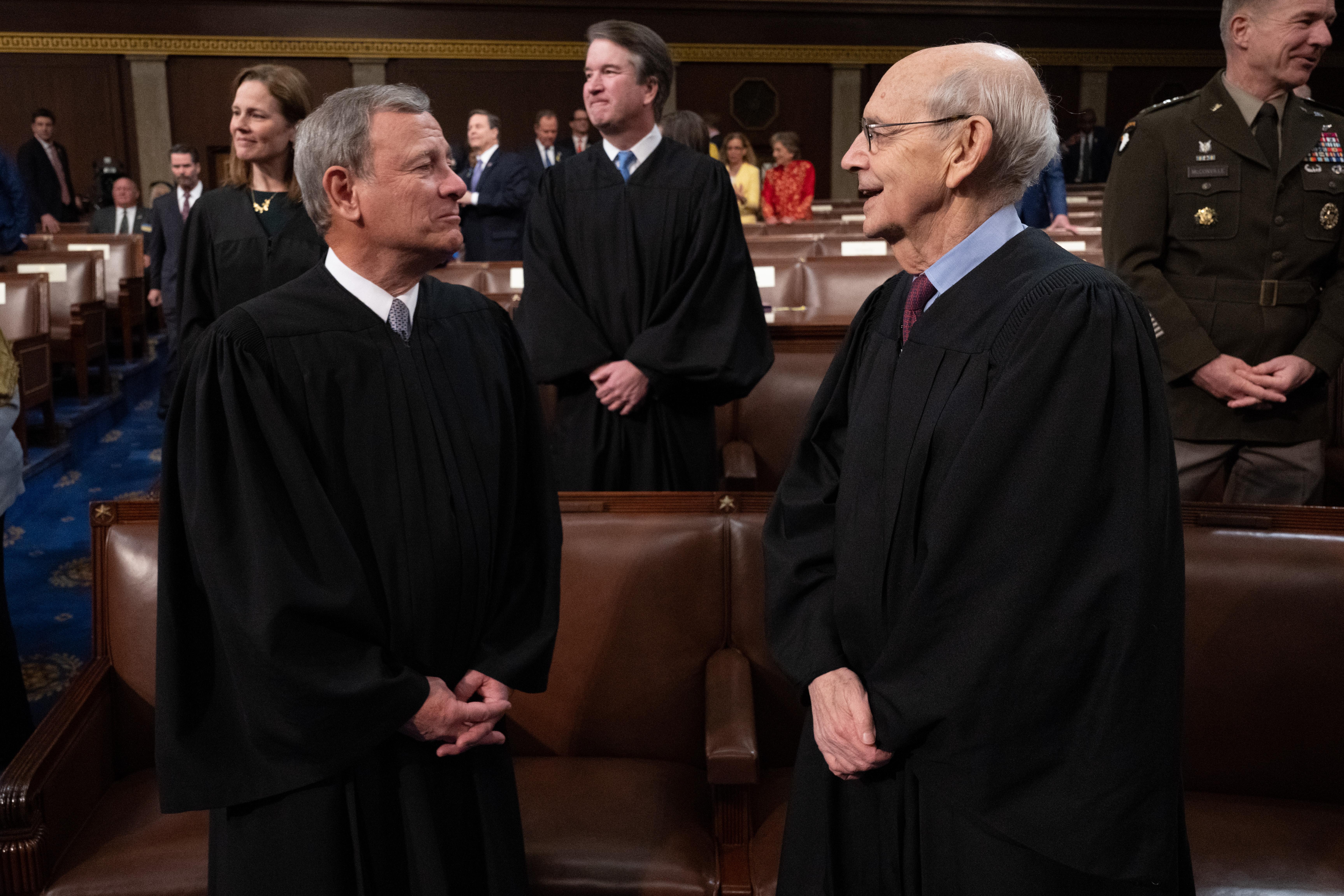 U.S. Supreme Court Chief Justice John Roberts speaks with retiring Justice Stephen Breyer at the State of the Union address by President Joe Biden. Both men are wearing their robes.