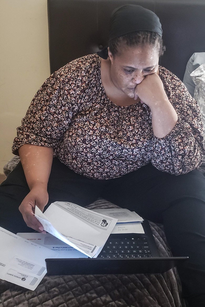 A woman sits in front of a laptop holding bills.