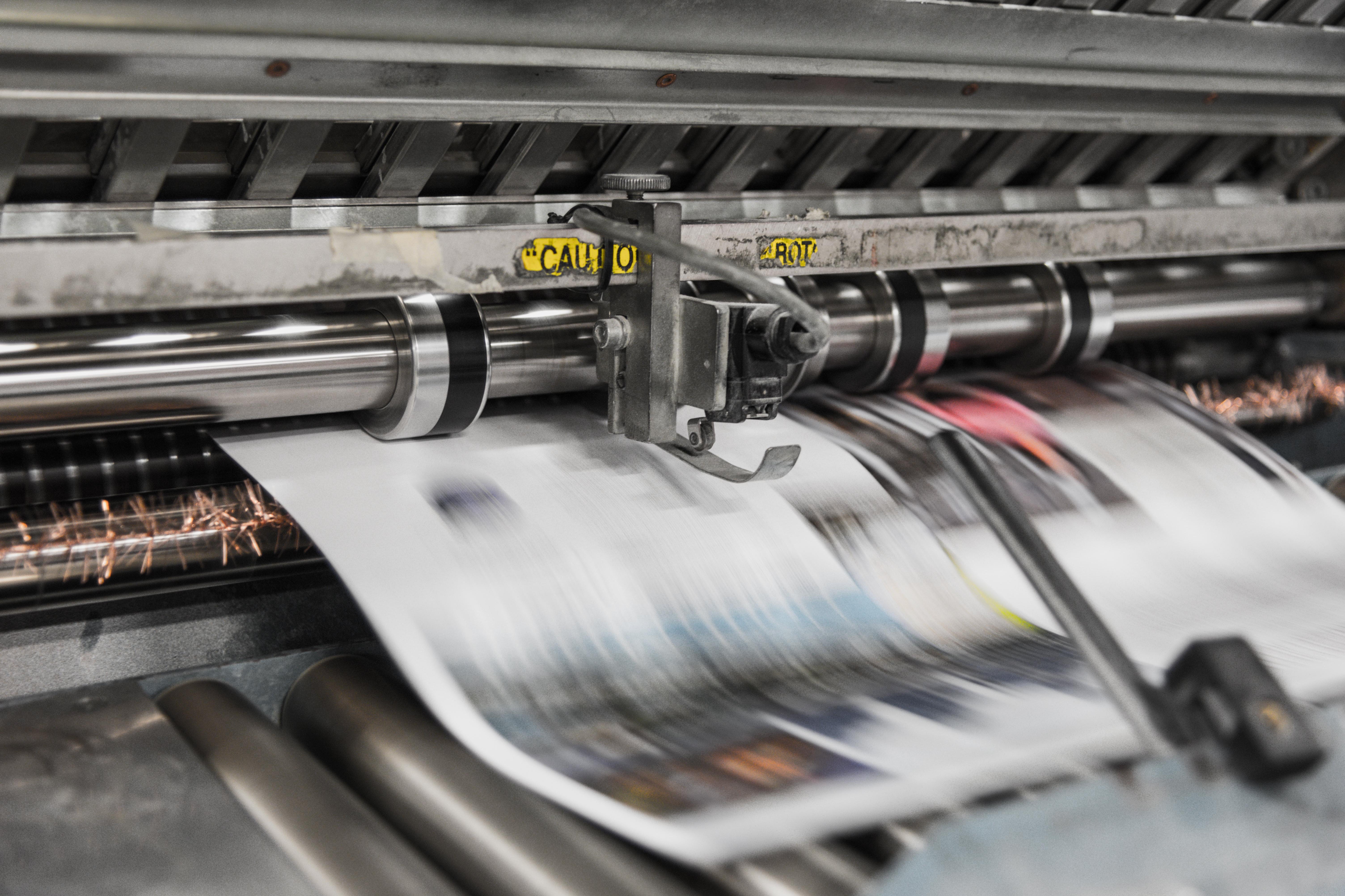 A blurry newspaper comes out of a printing press.