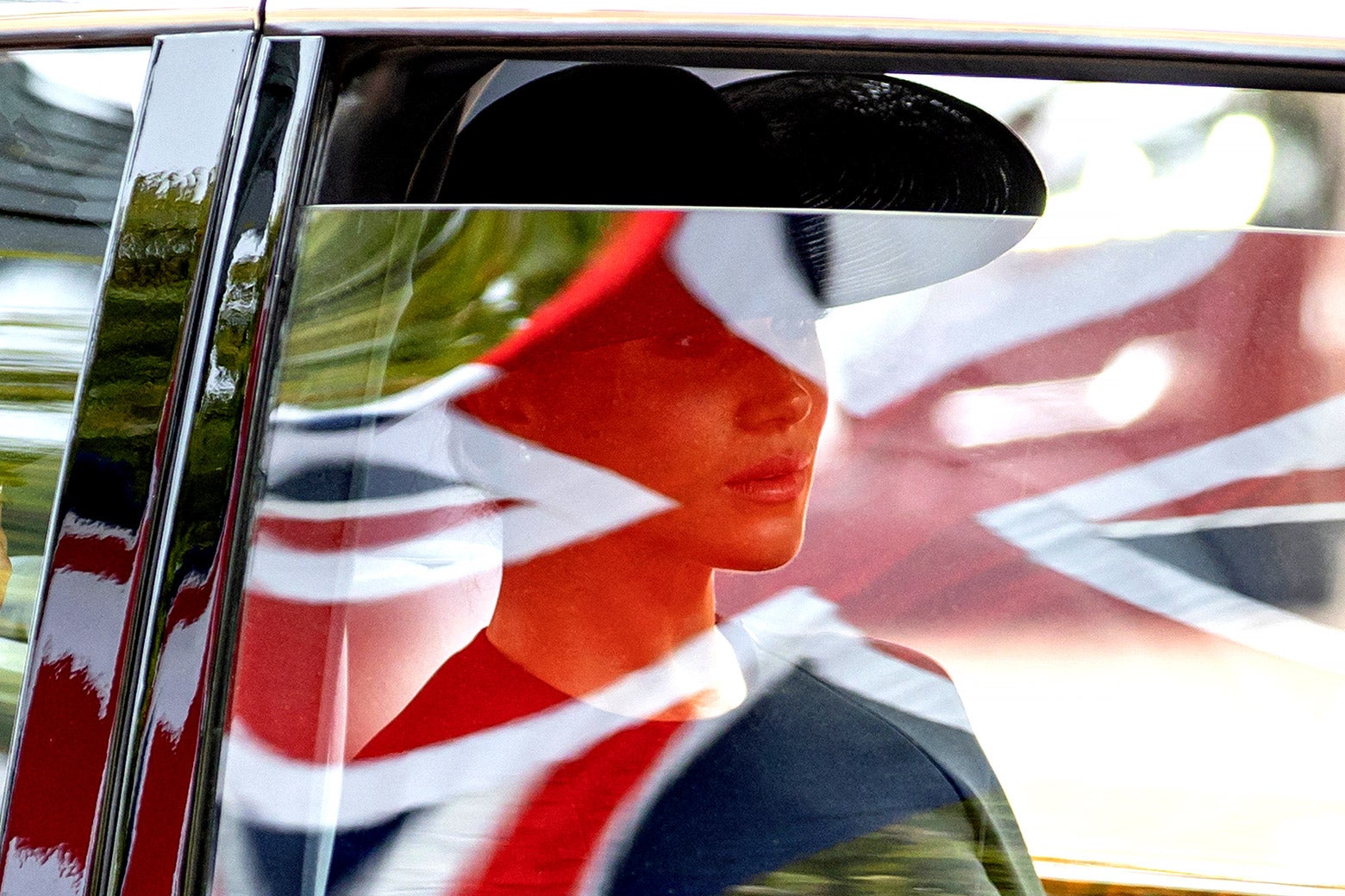 Meghan Markle seen through a car window, with a British flag superimposed.