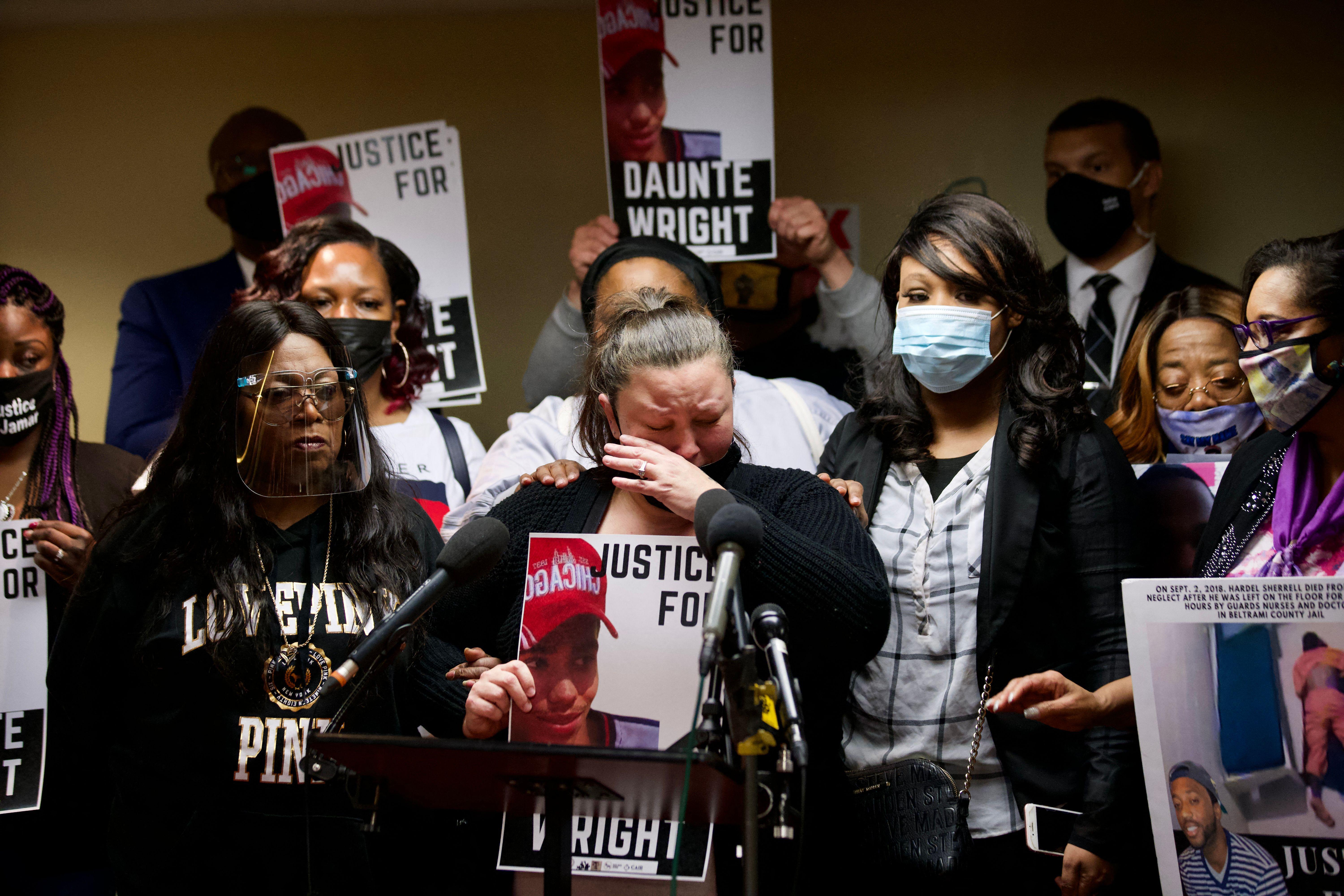 Katie Wright cries as she stands at a mic surrounded by supporters. Several, including Katie, are holding posters that say "Justice for Daunte Wright."