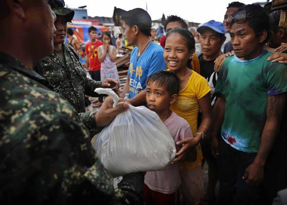 A young Filipino girl smiles as she and her brother receive their first bag of food aid at a center in Tacloban in the aftermath of Typhoon Haiyan on November 14, 2013 in Tacloban, Philippines. 