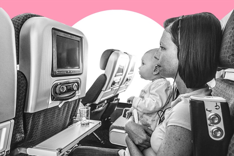 A woman watches a movie on a plane while she holds her baby on her lap.