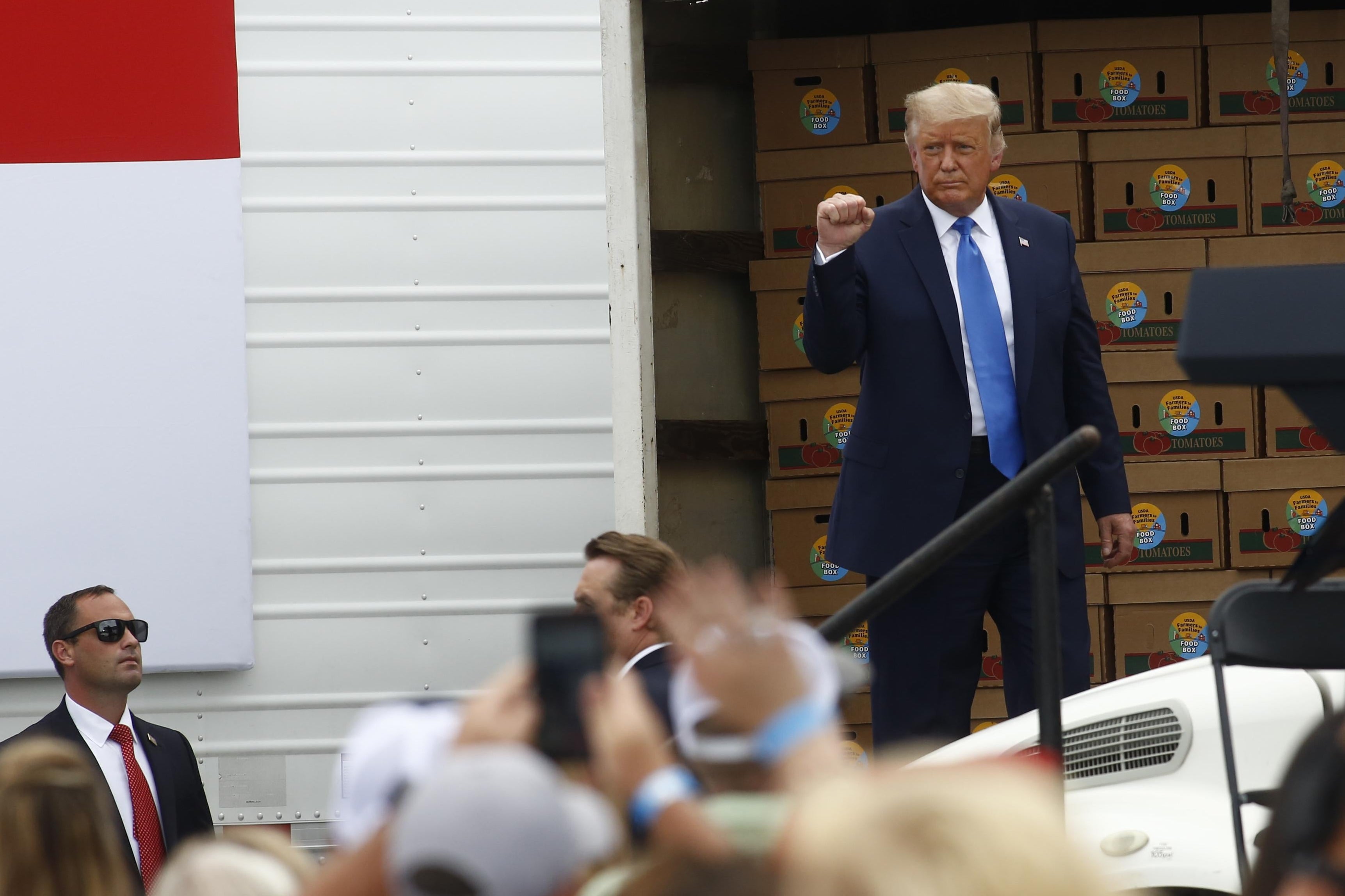 Trump stands in front of a truck full of food boxes.