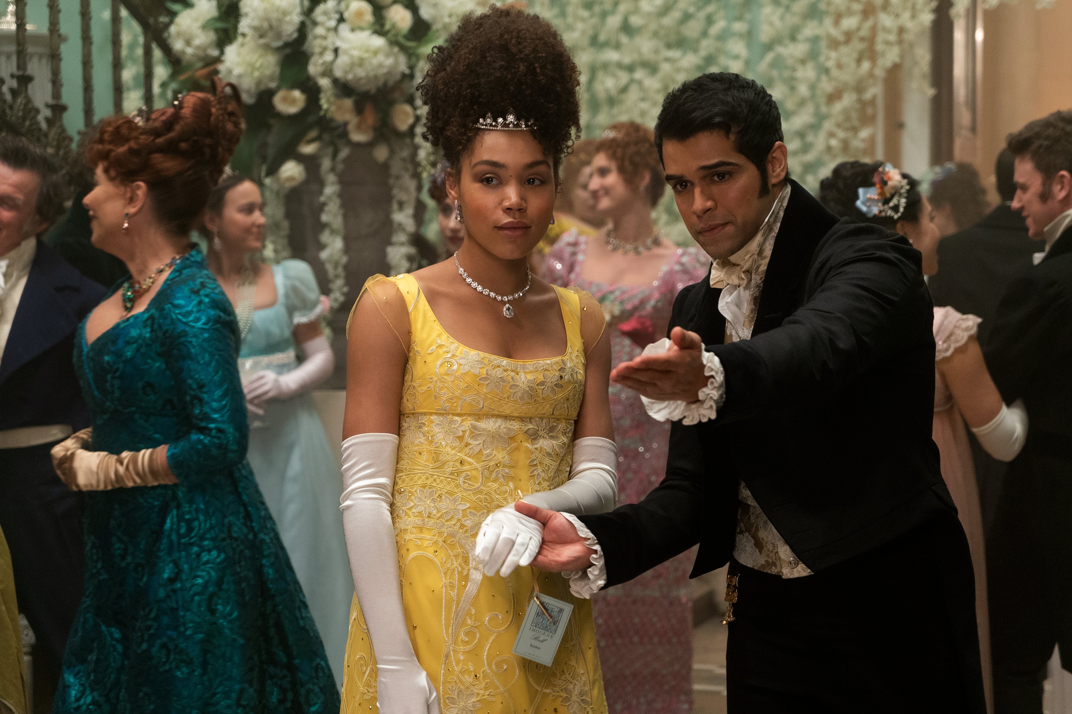 A man points and holds Ruby Barker's gloved hand in a crowded ballroom.