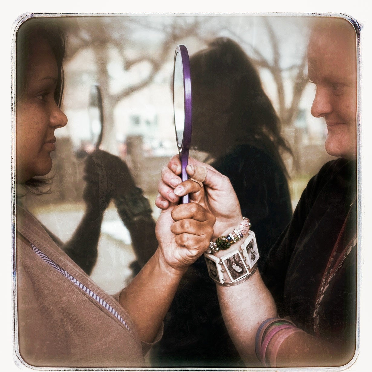 Two women hold a handheld mirror. This image appears in the book EXPOSURE: Homelessness through the lens of art & poetry.