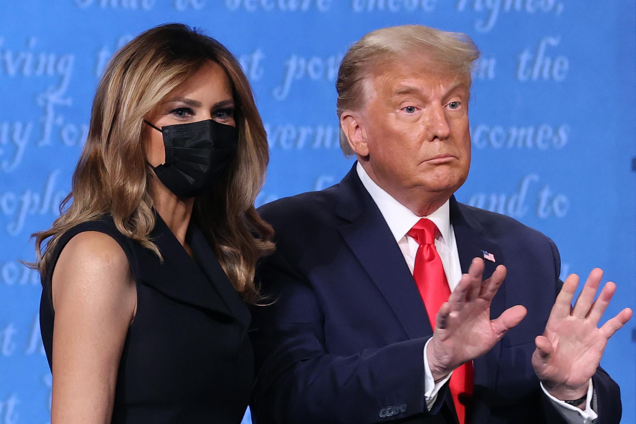 Trump holds up both his hands while standing next to Melania, who's wearing a mask, on the debate stage following the final presidential debate.
