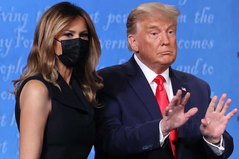 Trump holds up both his hands while standing next to Melania, who's wearing a mask, on the debate stage following the final presidential debate.