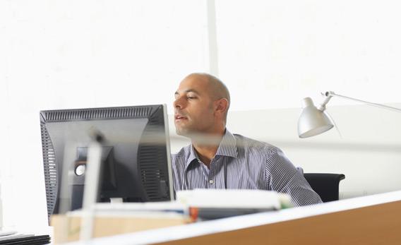 Businessman peering over computer monitor.