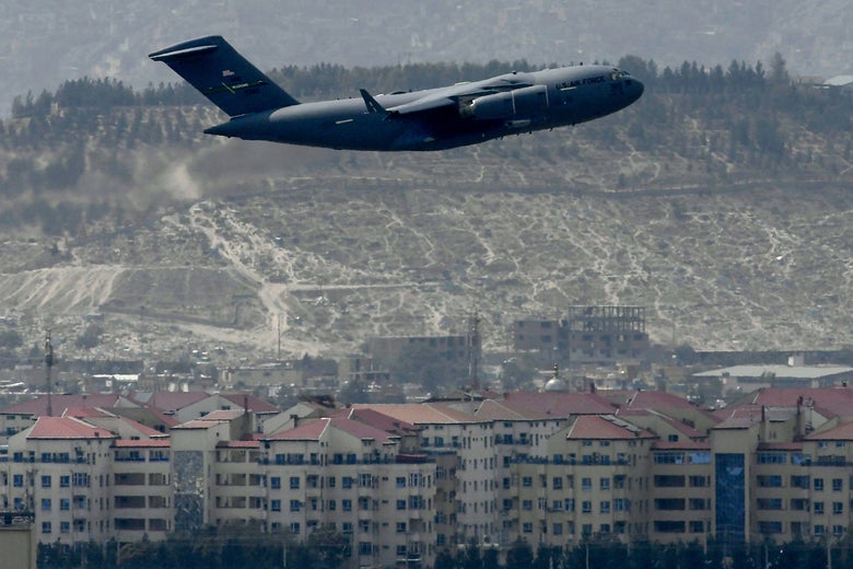 An airplane in flight above buildings with mountains in the background
