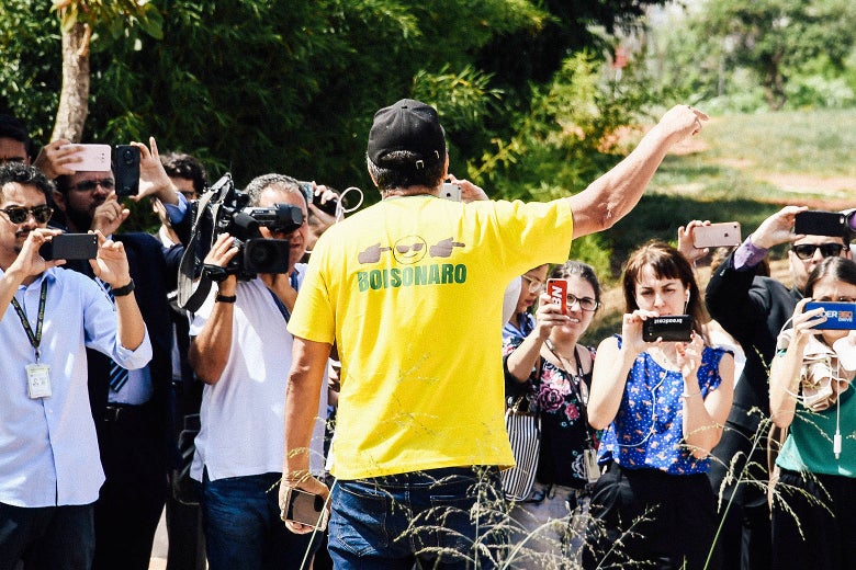 A man in a T-shirt that says Bolsonaro points and yells at reporters.